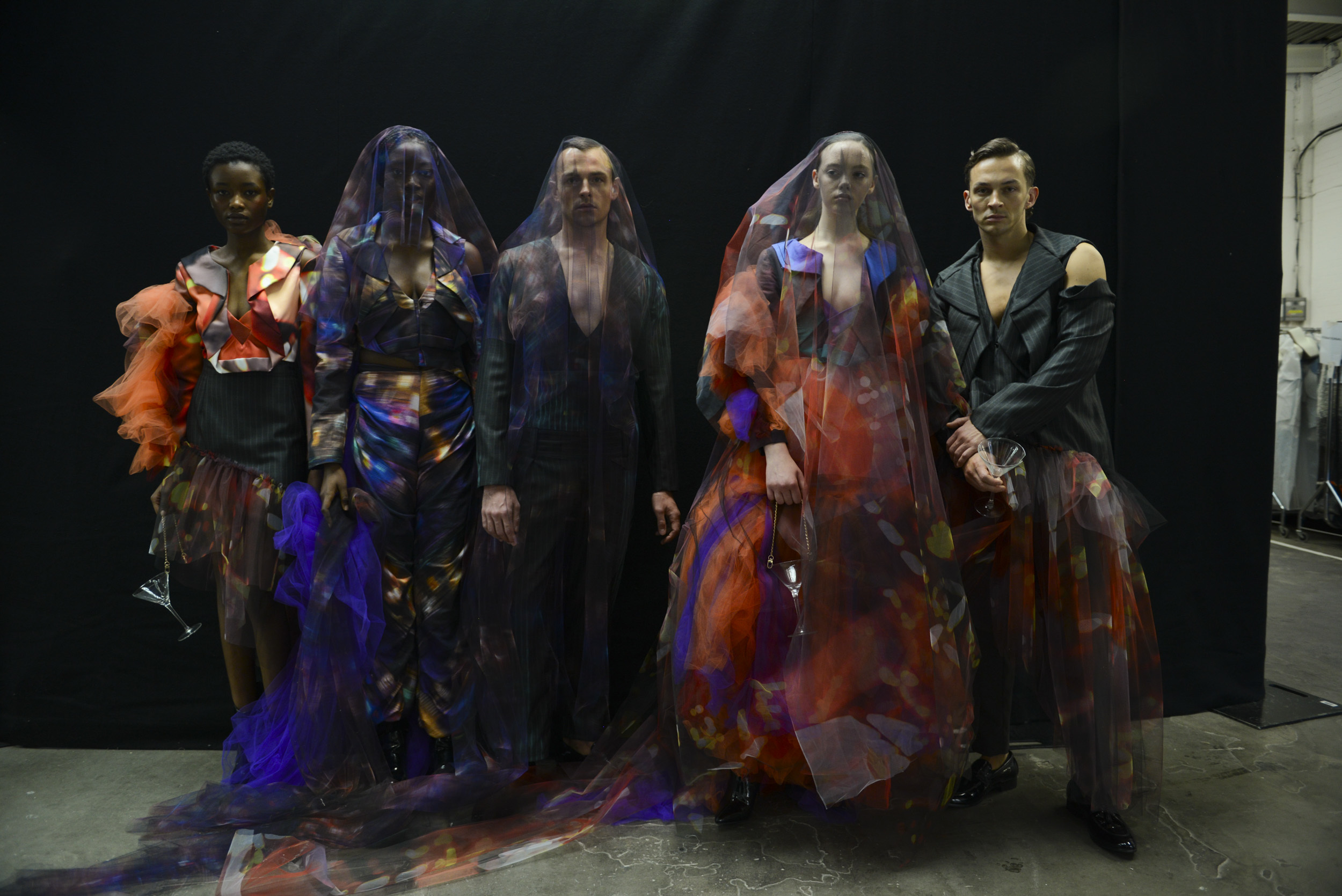 Five models lined up backstage at Graduate Fashion Week wearing dark and colourful outfits and veils designed by a BA (Hons) Fashion student.