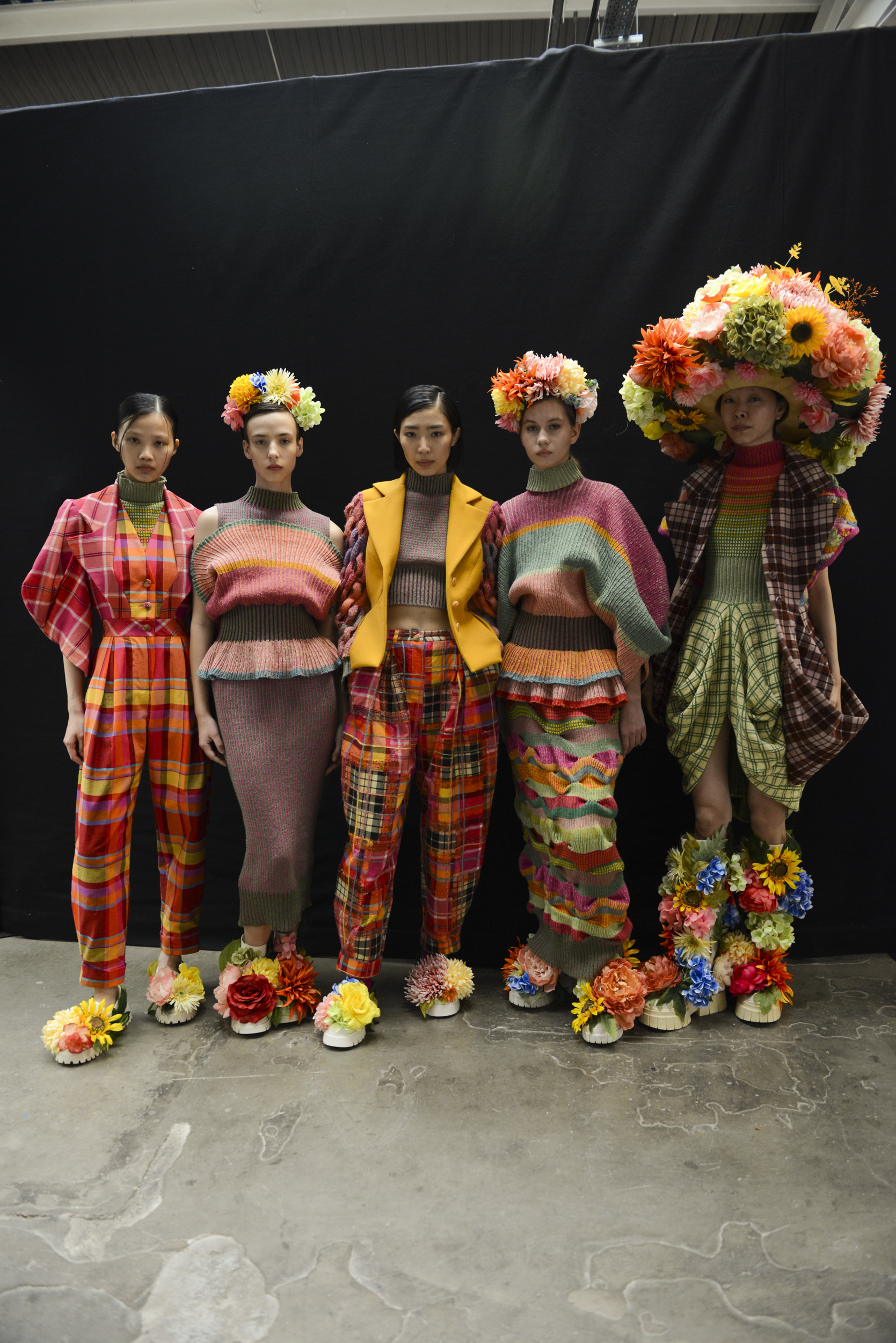 Five models lined up backstage at Graduate Fashion Week 2024, wearing colourful clothing with flower accessories and motifs.