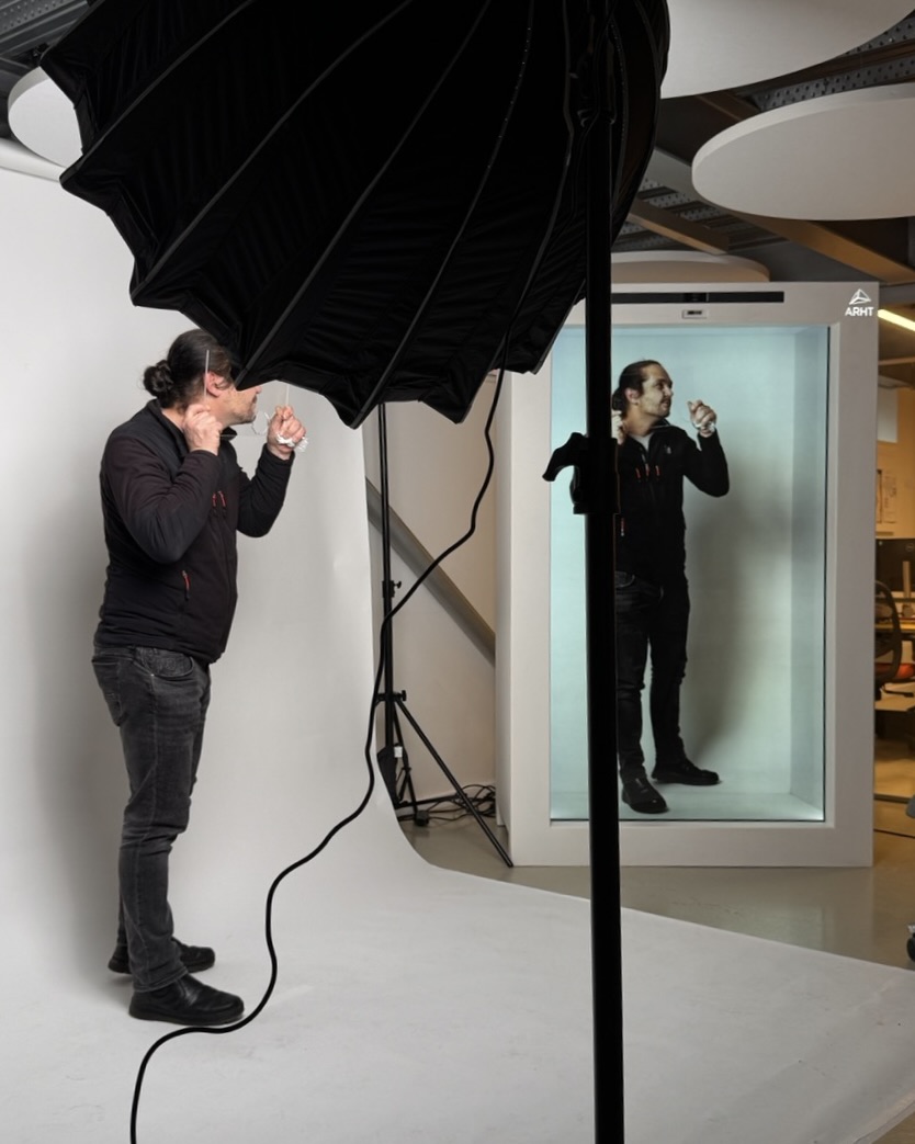 Staff member posing in front of white background, to the right is a hologram projection of him in the Holobox, wires and frames in between.