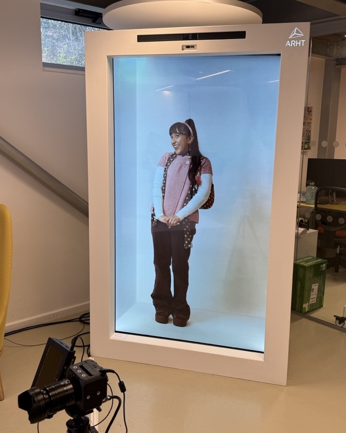 Hologram projection of student stood on a white background in Holobox, wearing white top, jeans and white sleeves.