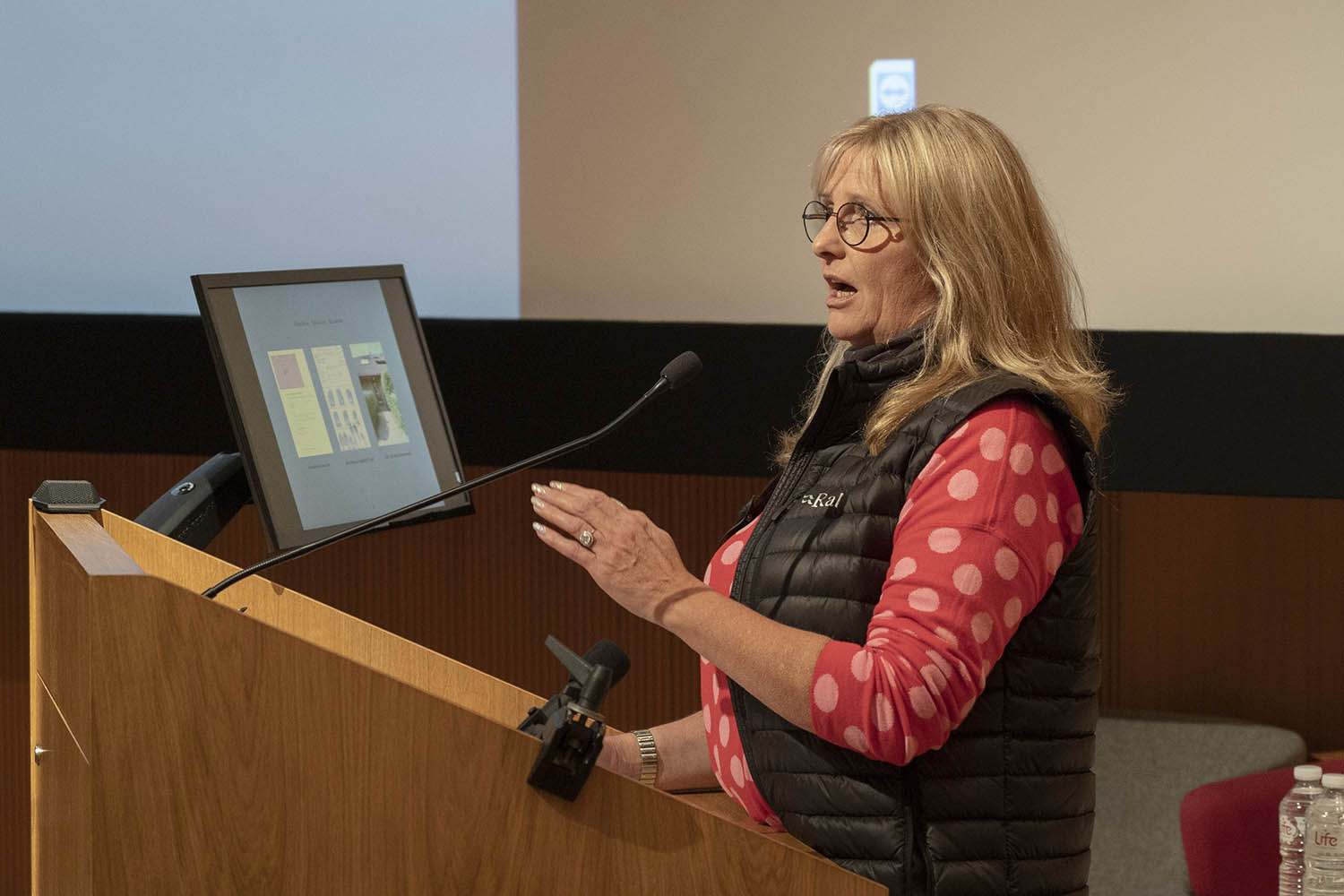 Artist K Cox standing at a lectern in the middle of a speech.