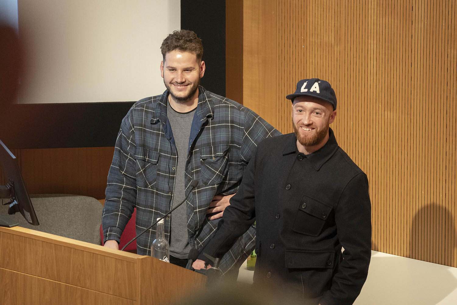 Two people standing at a lectern in a lecture theatre smiling at the audience.
