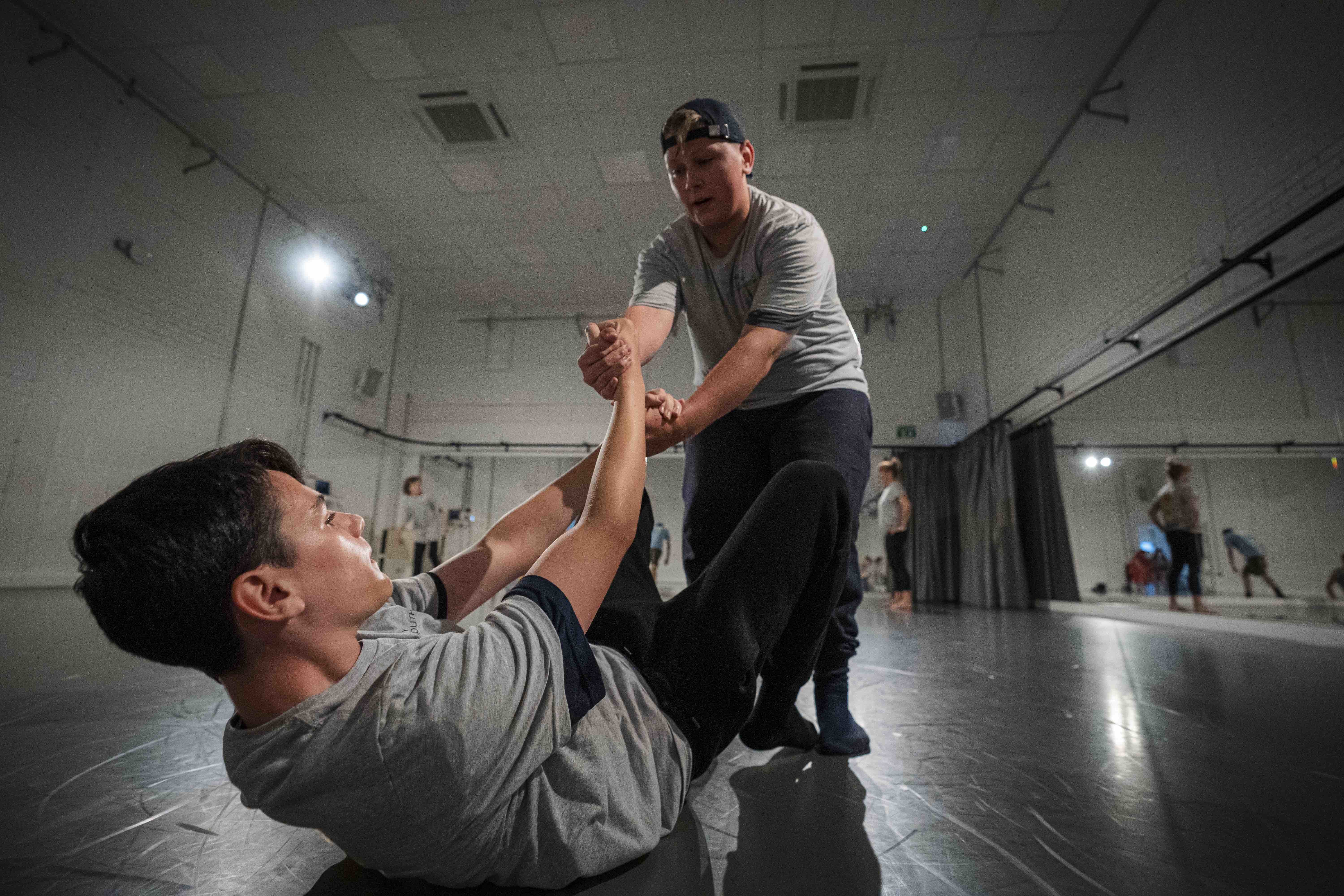 One person leans over and helps another person off of the ground with both hands.