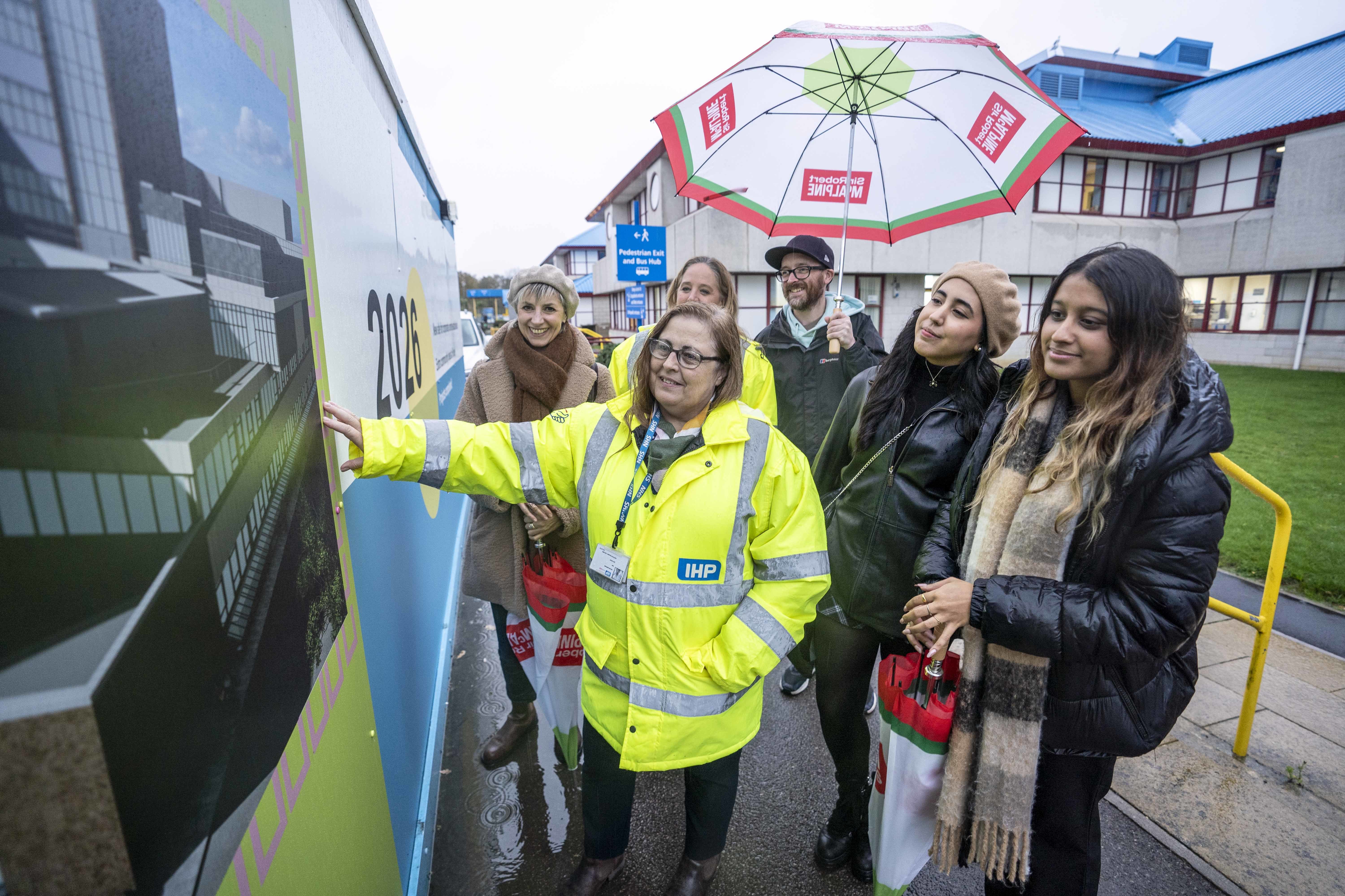 Students and staff from BA (Hons) Interior Architecture and Design look at their new design work at Royal Bournemouth Hospital. Six people stand smiling at a vehicle parked outside a hospital.