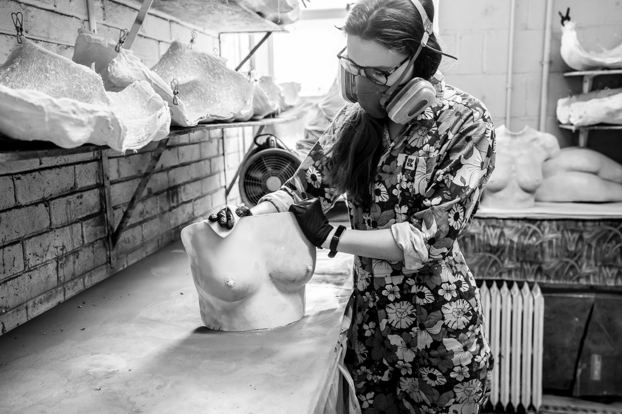 Lydia Reeves working on a vulva cast in her studio, wearing flowery Lucy & Yak overalls and mask with a filter.