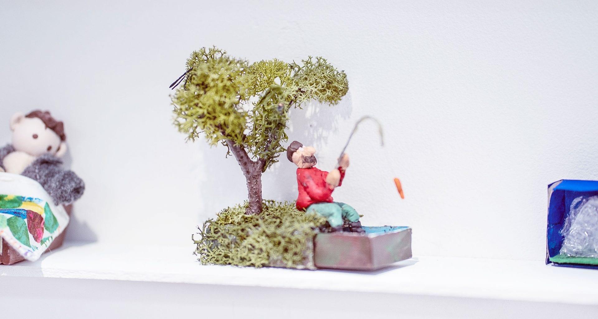 Miniature sculpture of a man fishing under a tree.