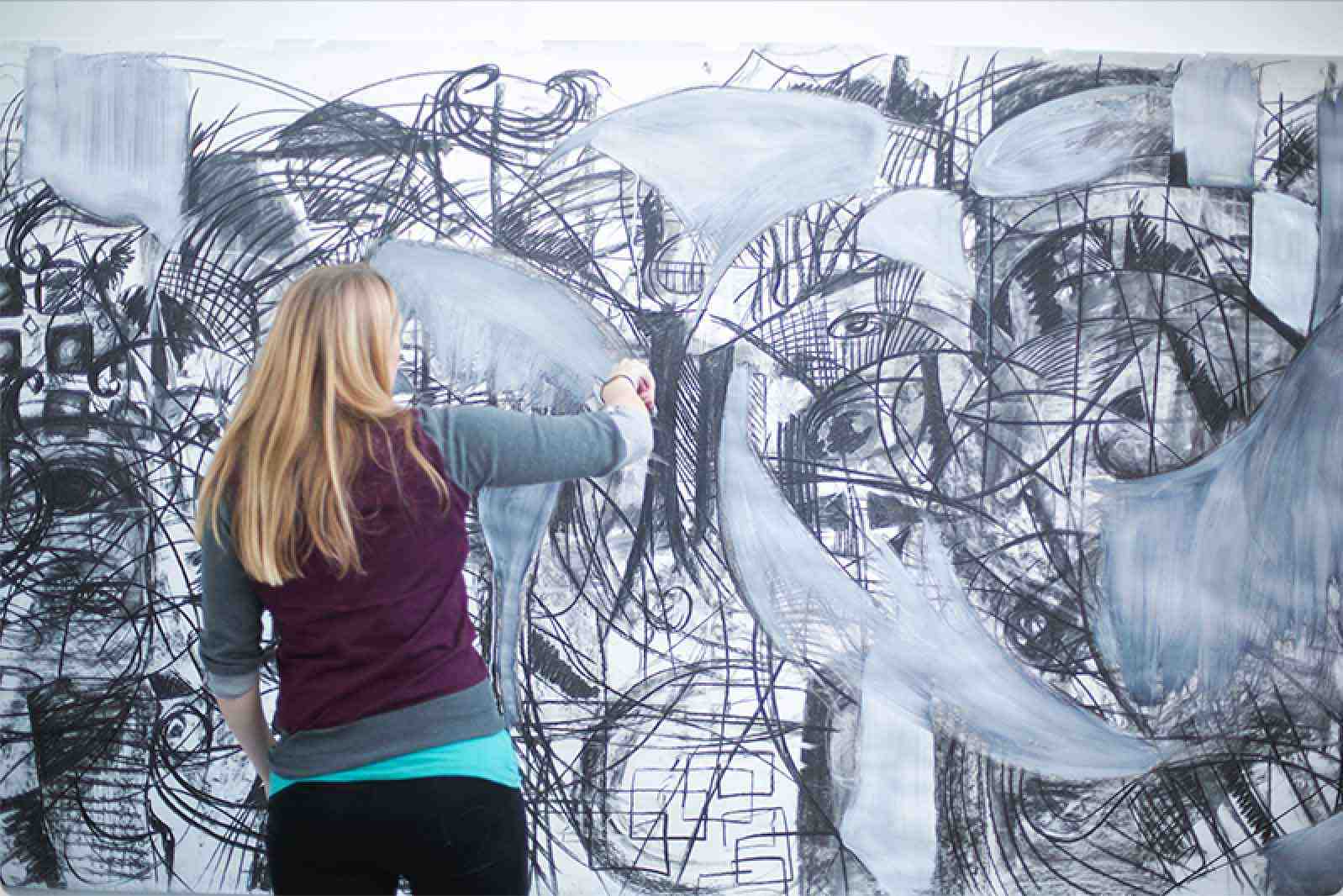 An AUB student working on an abstract artwork across an entire wall.