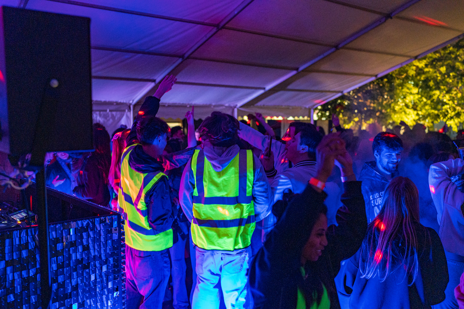 A large group of students, some wearing hi-vis vests on a crowded dance floor.