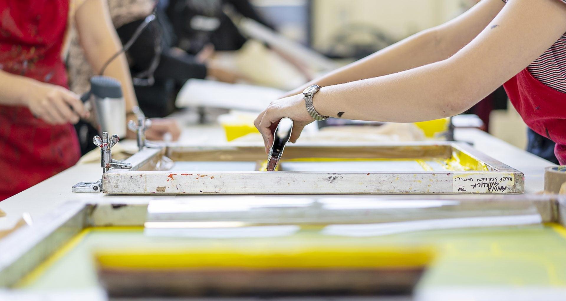 A person uses screen printing equipment on a long table.