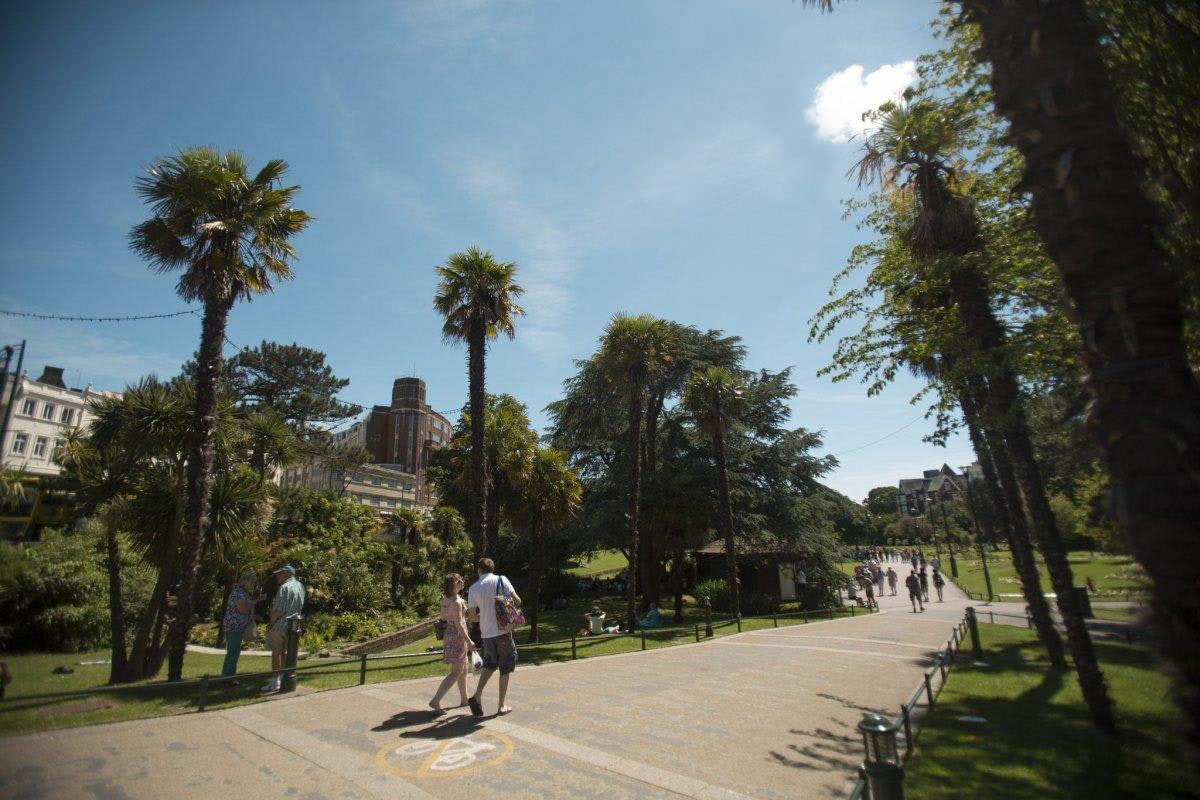 People walking through sunny gardens, a hot air balloon is up in the distance