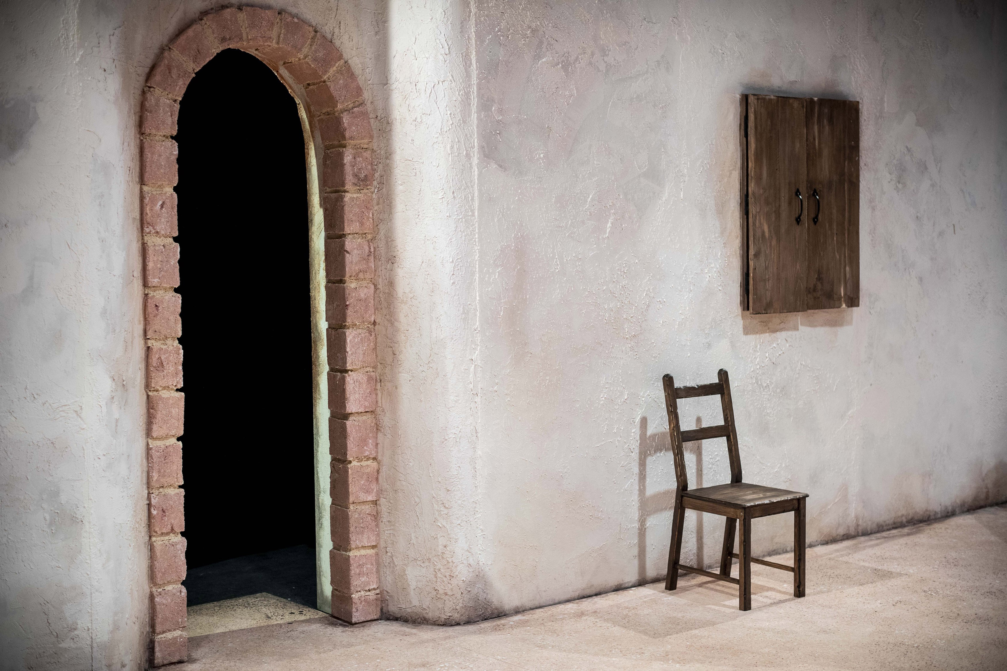 A room with a brick arch doorway towards the left. A chair is by the wall with a picture hanging up to the right.