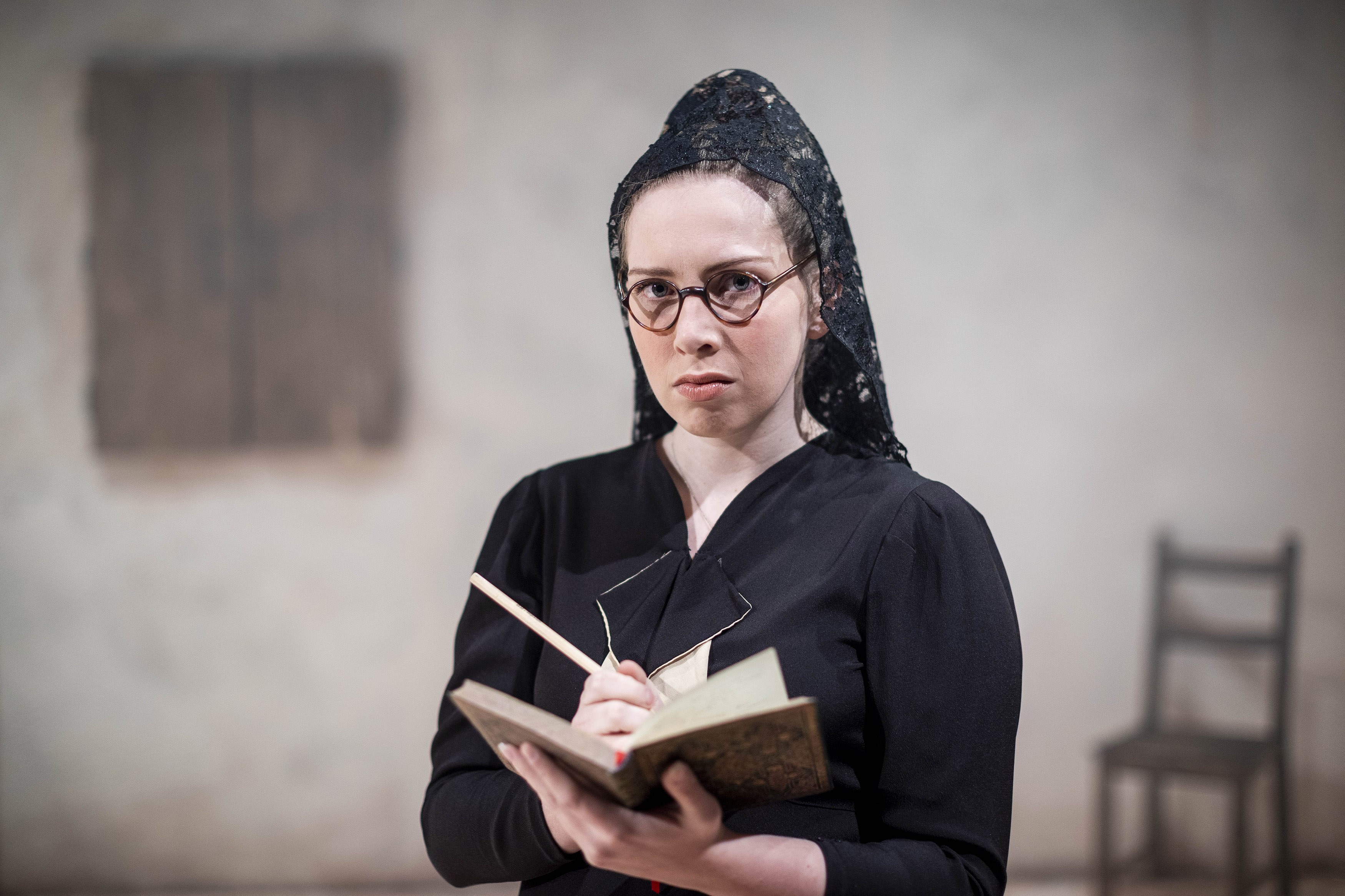 A person with a serious expression holds a book and writes in it.