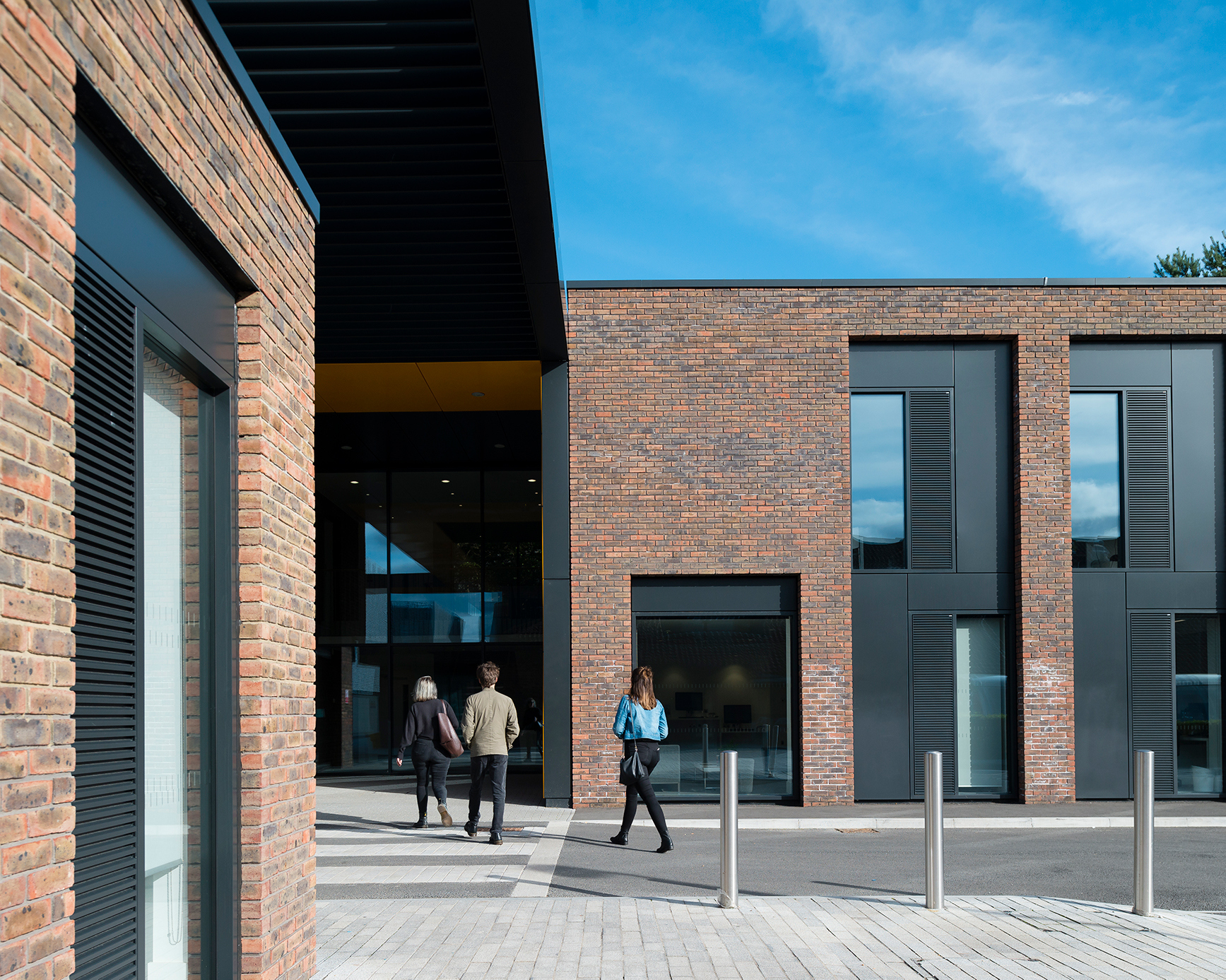 Three students crossing a road to walk into a brick university building with large windows.