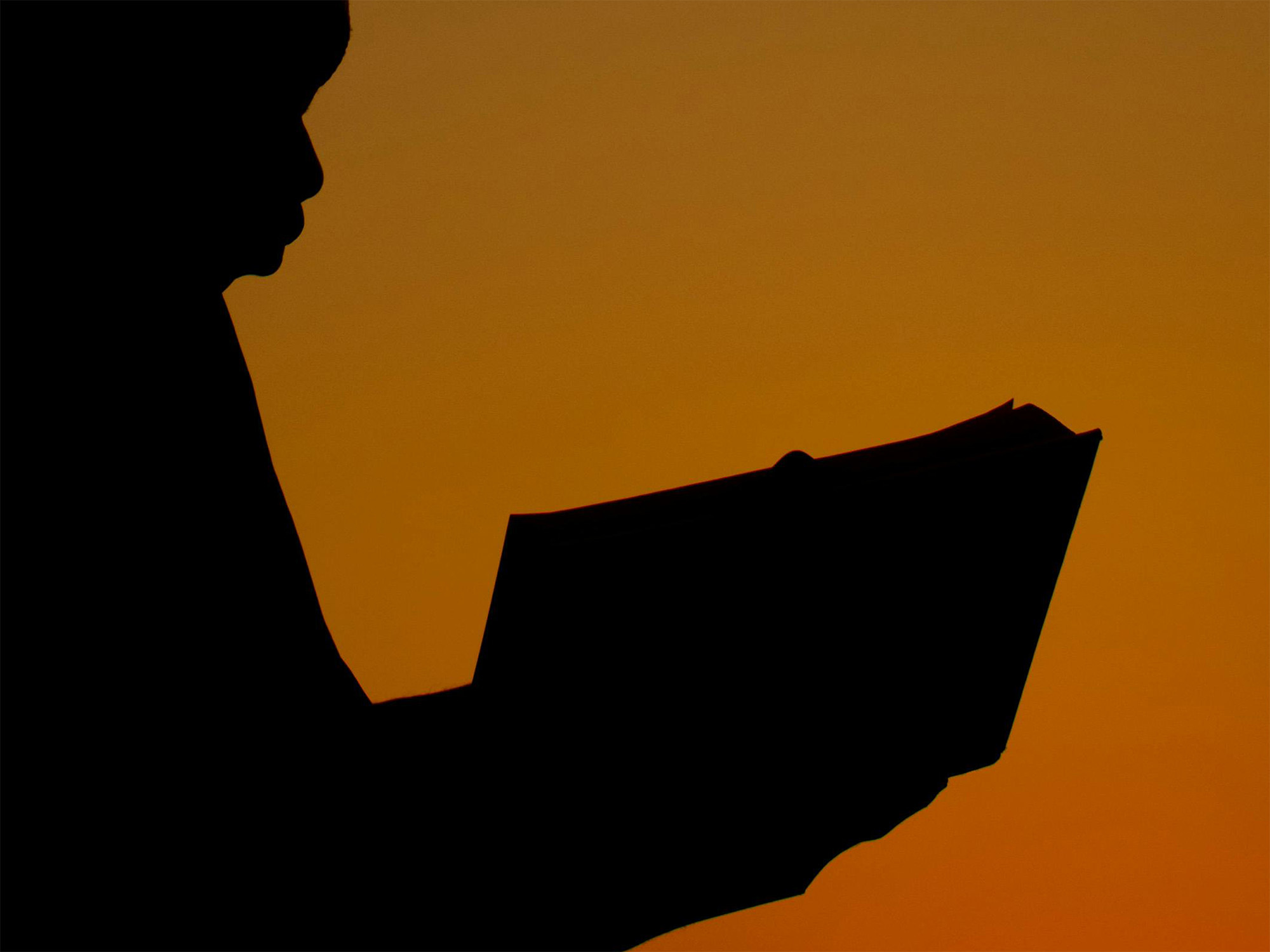 A silhouette of a person reading, set against a orange and gold background.
