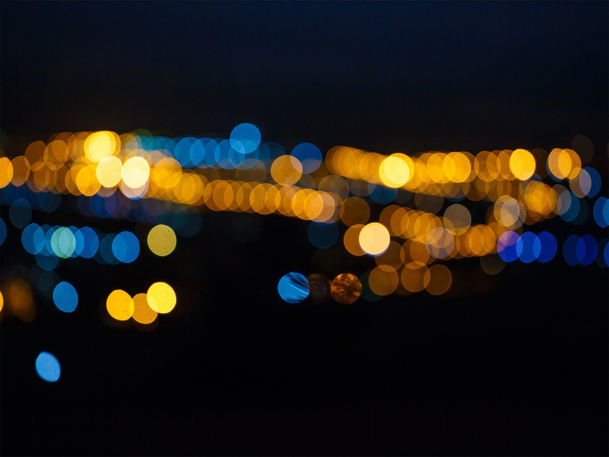 A primarily black, blue and gold abstract image resembling blurred lights viewed in the distance.