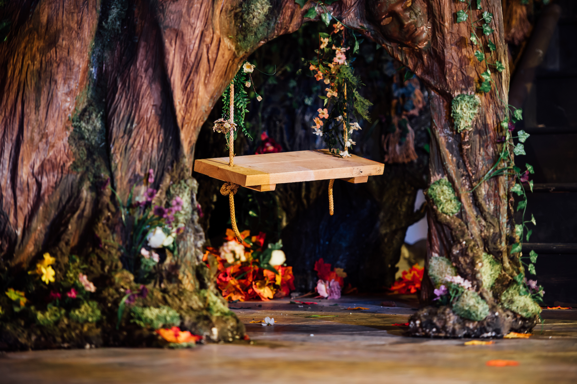 Set design for A Midsummer Night's Dream with a wooden swing under a tree arch with foliage.