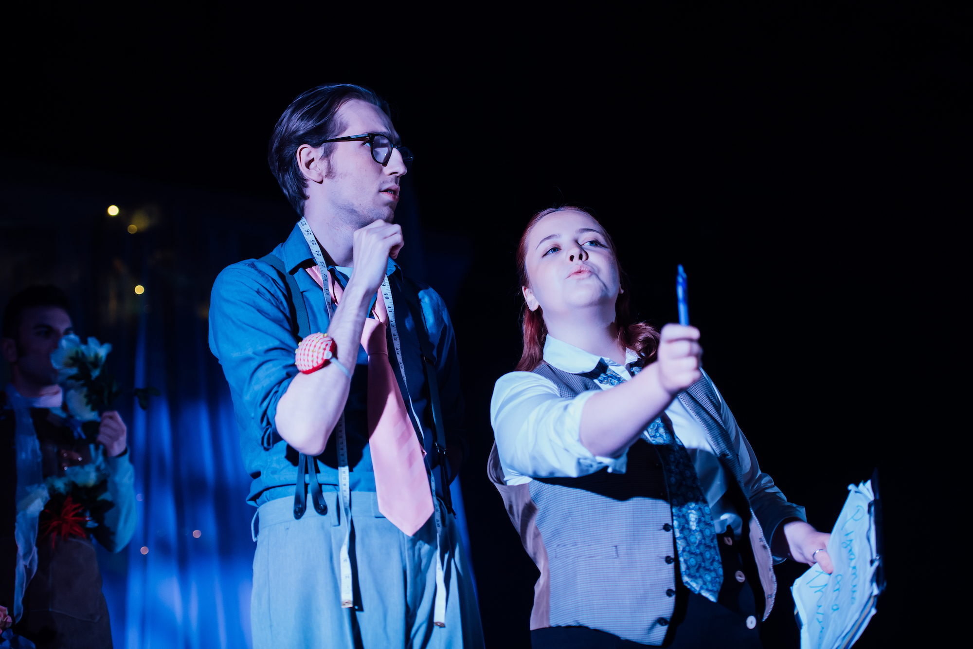 Actors on stage in A Midsummer Night's Dream dressed as tailors in blue lighting.