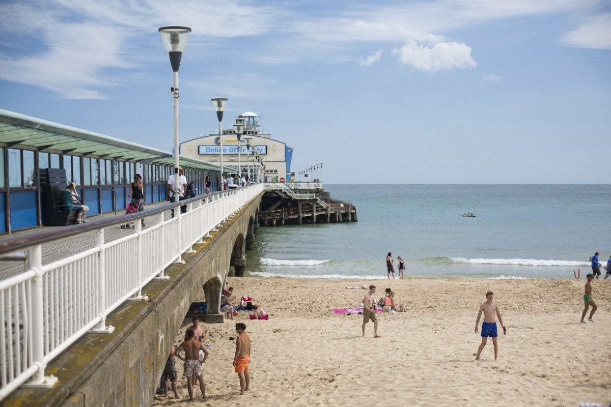 Bournemouth Pier jutting out into the water, groups of people playing on the sand to the right of the pier.
