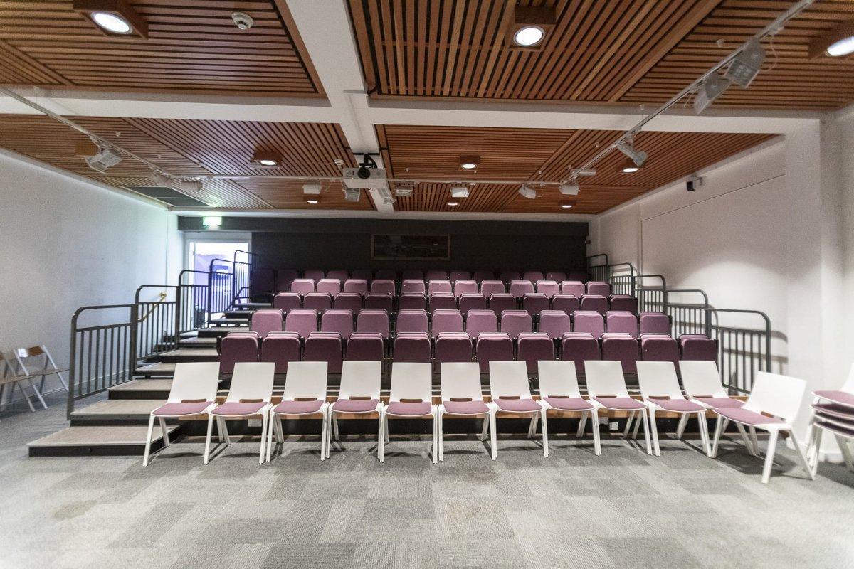 Several rows of empty seats and a set of stairs on the left-hand side in a lecture theatre.