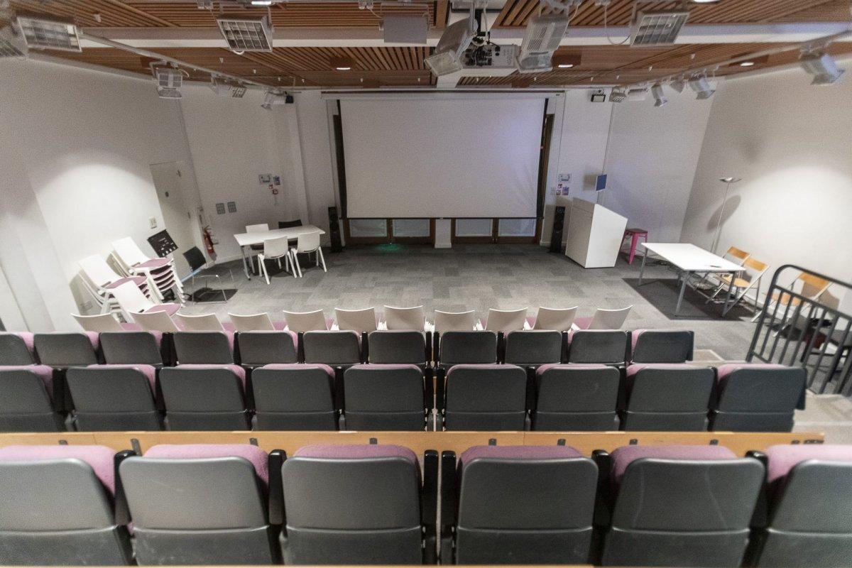 Empty lecture theatre viewed from an upper row of seating, with lower rows of seats visible in the foreground.