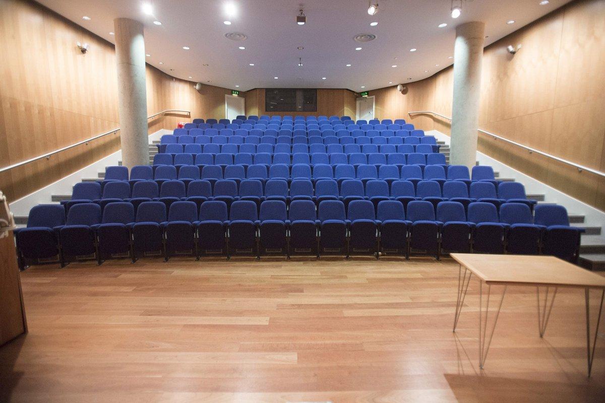 Ten rows of empty seating viewed from the front of a large lecture theatre.