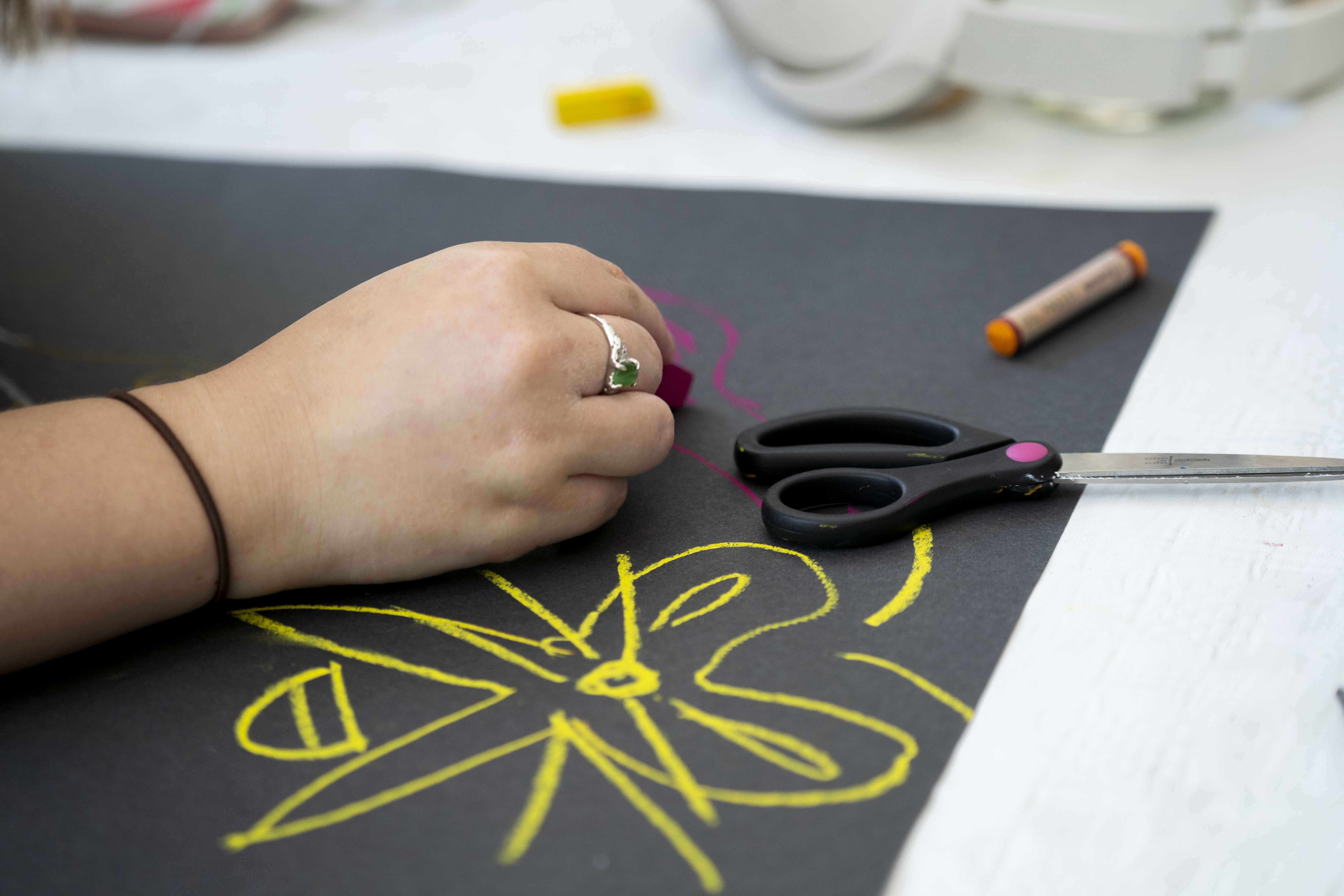 A Summer School student's hand drawing flowers in bright yellow on black card