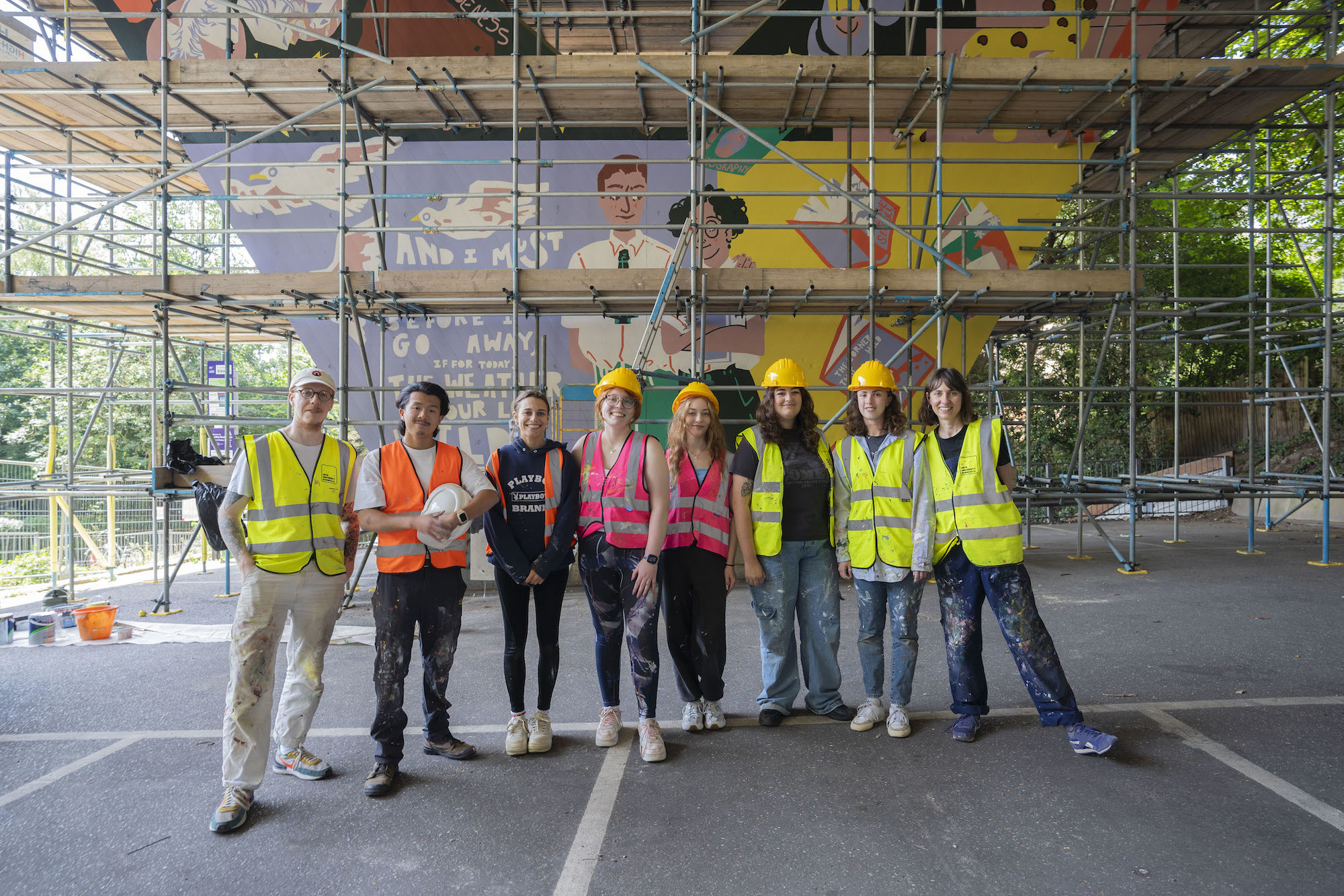 Artists posing in front of the colourful mural at Braidley Road wearing different coloured high-vis.
