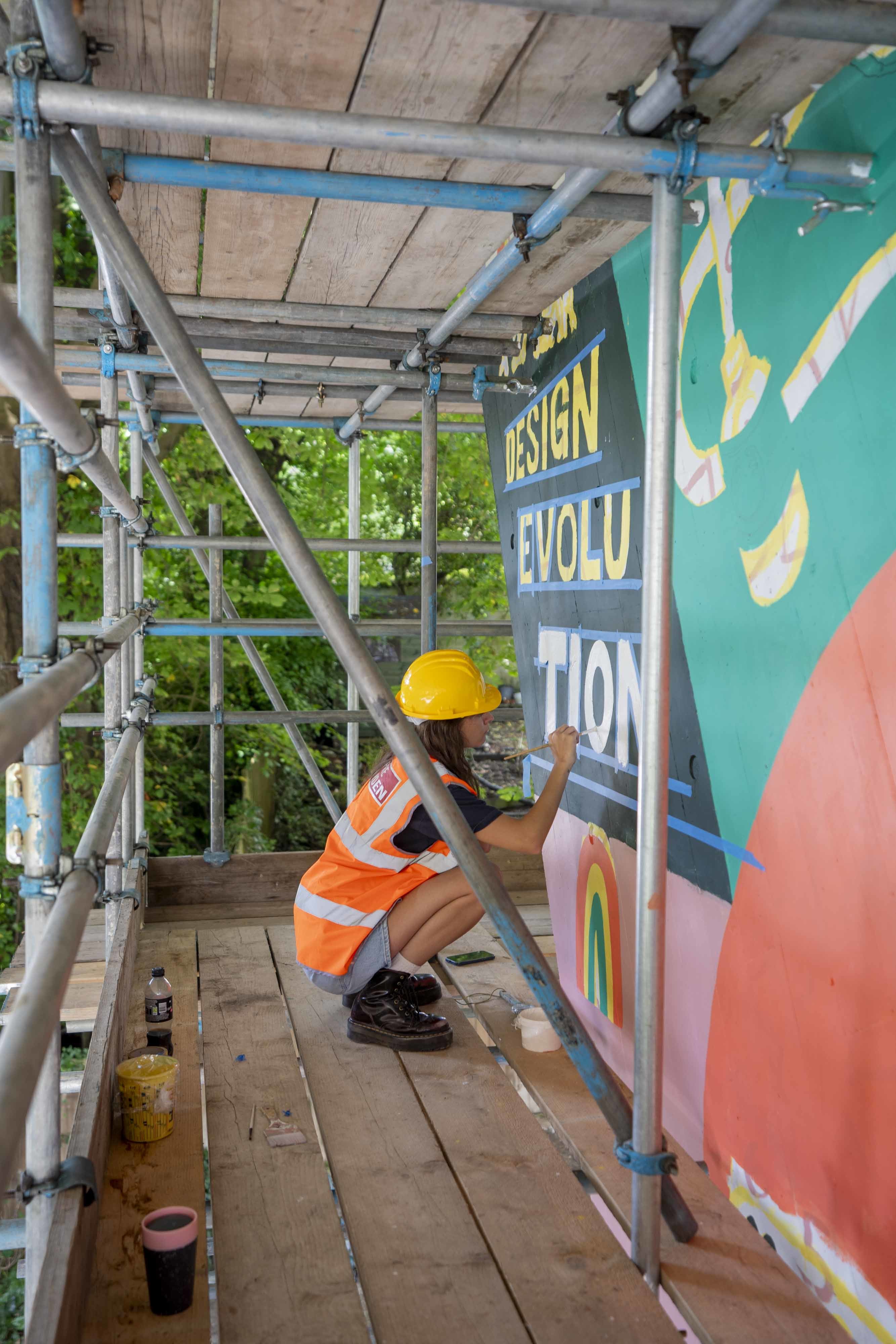 A student in hi-vis and construction hat working on the Braidley Rd. mural.