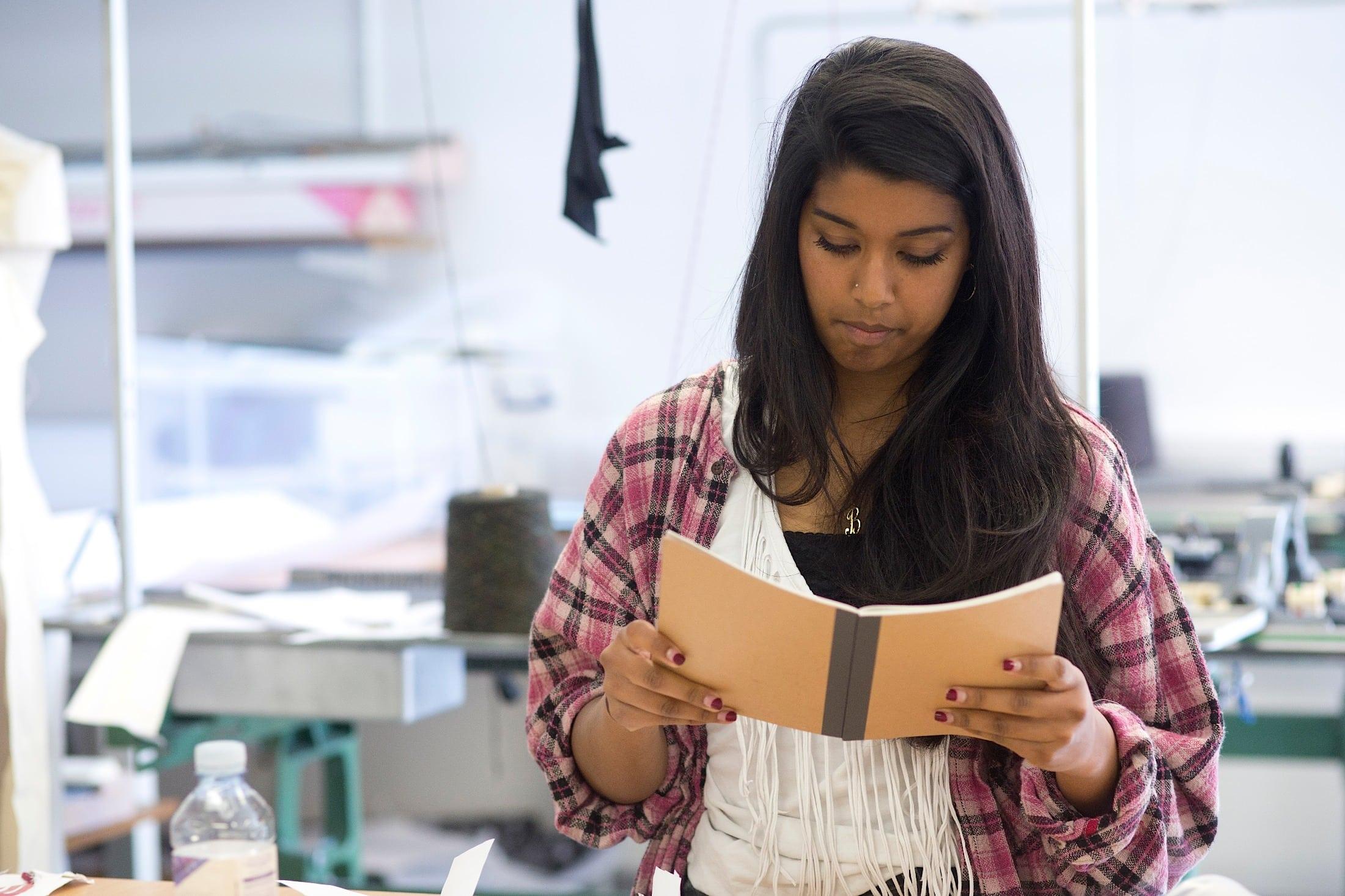 Student standing in a studio and reading from an exercise book.