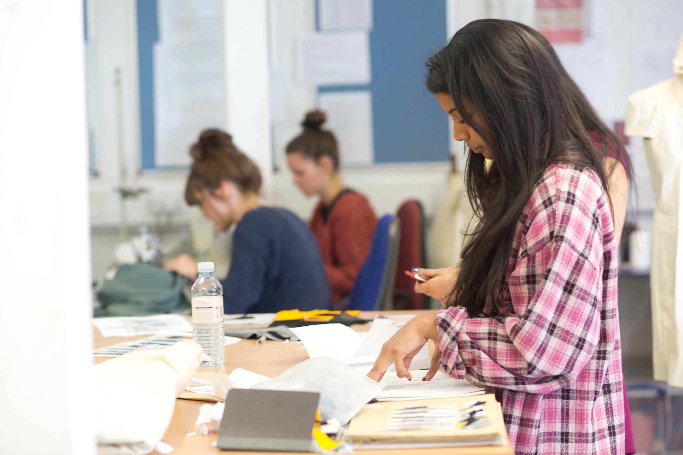 Student standing by a table in a studio, looking down and working on a project.