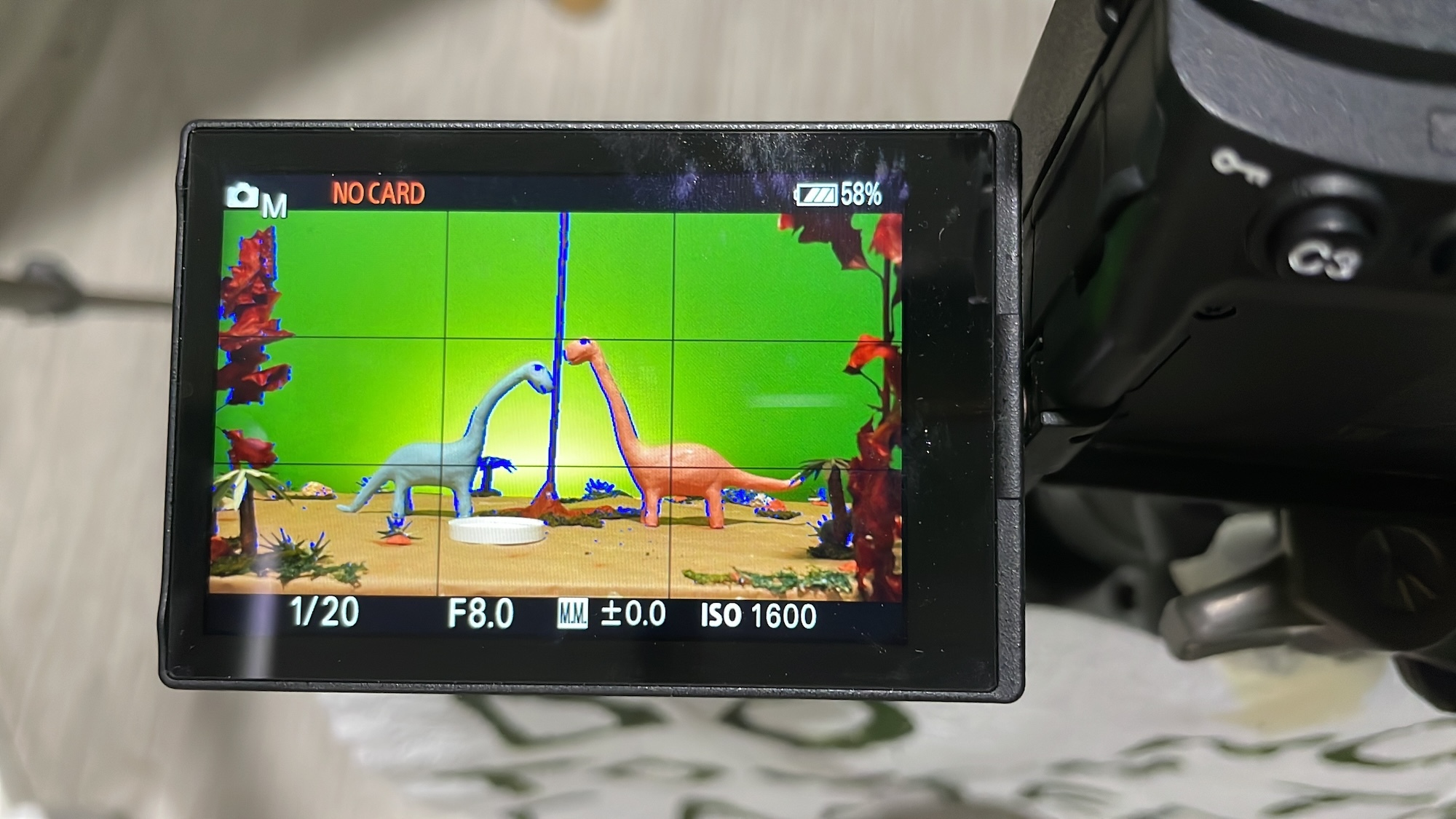 Close-up of a camera's monitor showing two animated dinosaurs on a green screen background.