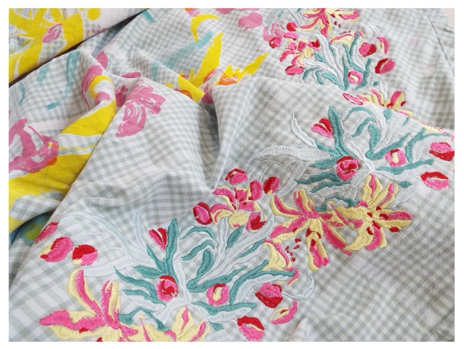 Crumpled fabric with grey gingham pattern and floral print in pink, yellow, and green tones scattered across surface.