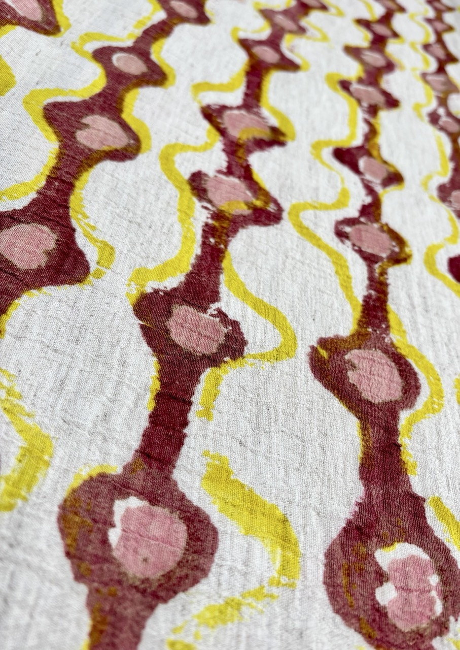 Abstract fabric pattern with curved burgundy shapes containing pink oval spots, outlined in yellow on white background.