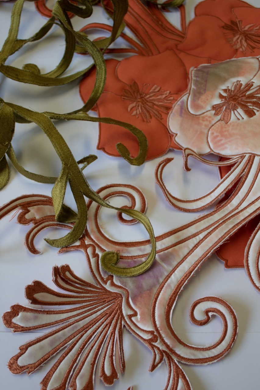 Flowing fabric with large orange lilies and green scrolling vines on white background, creating swirling botanical pattern.