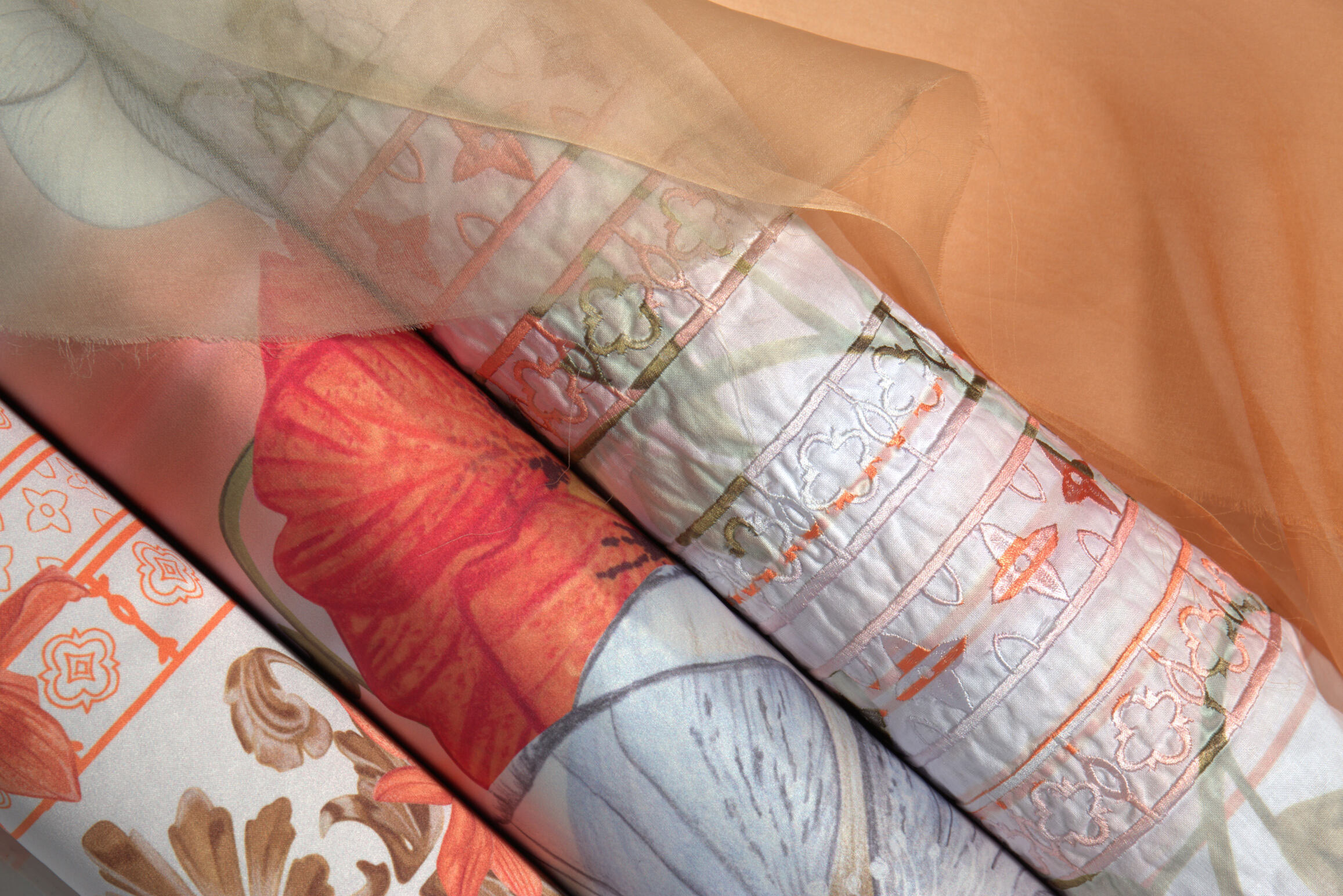 Folded quilts with patchwork patterns in coral, pink, grey, and white fabrics stacked on wooden surface.