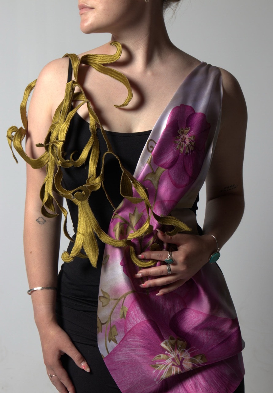 Woman in black top holding yellow ribbons, draped in purple floral fabric against grey background.