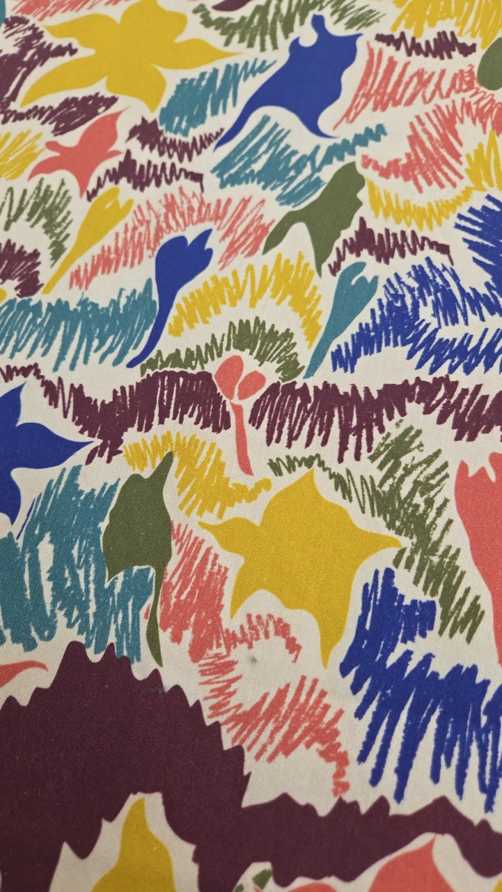 A close-up of a textured surface featuring a vibrant pattern of abstract shapes in various colours including pink, blue, yellow, green, and purple. The design is made up of wavy lines and organic forms, creating a lively visual effect.