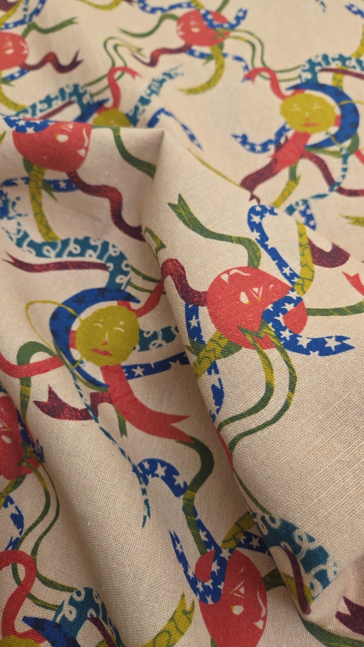 A close-up of patterned fabric featuring multicoloured designs of smiling, playful octopuses with long tentacles and vibrant coloured elements on a light beige background. The fabric appears slightly wrinkled.