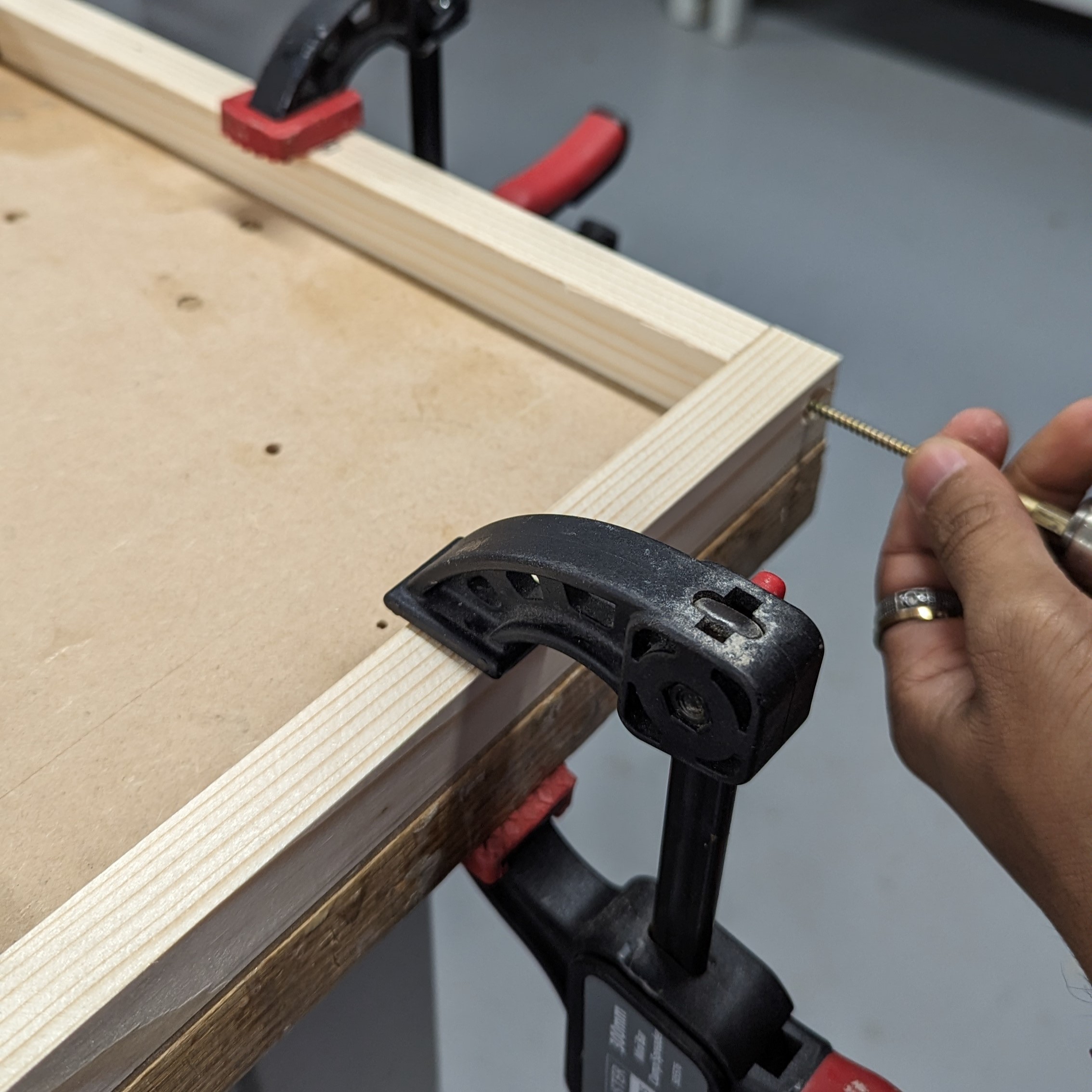The corner of a wooden frame held in place by two vices.