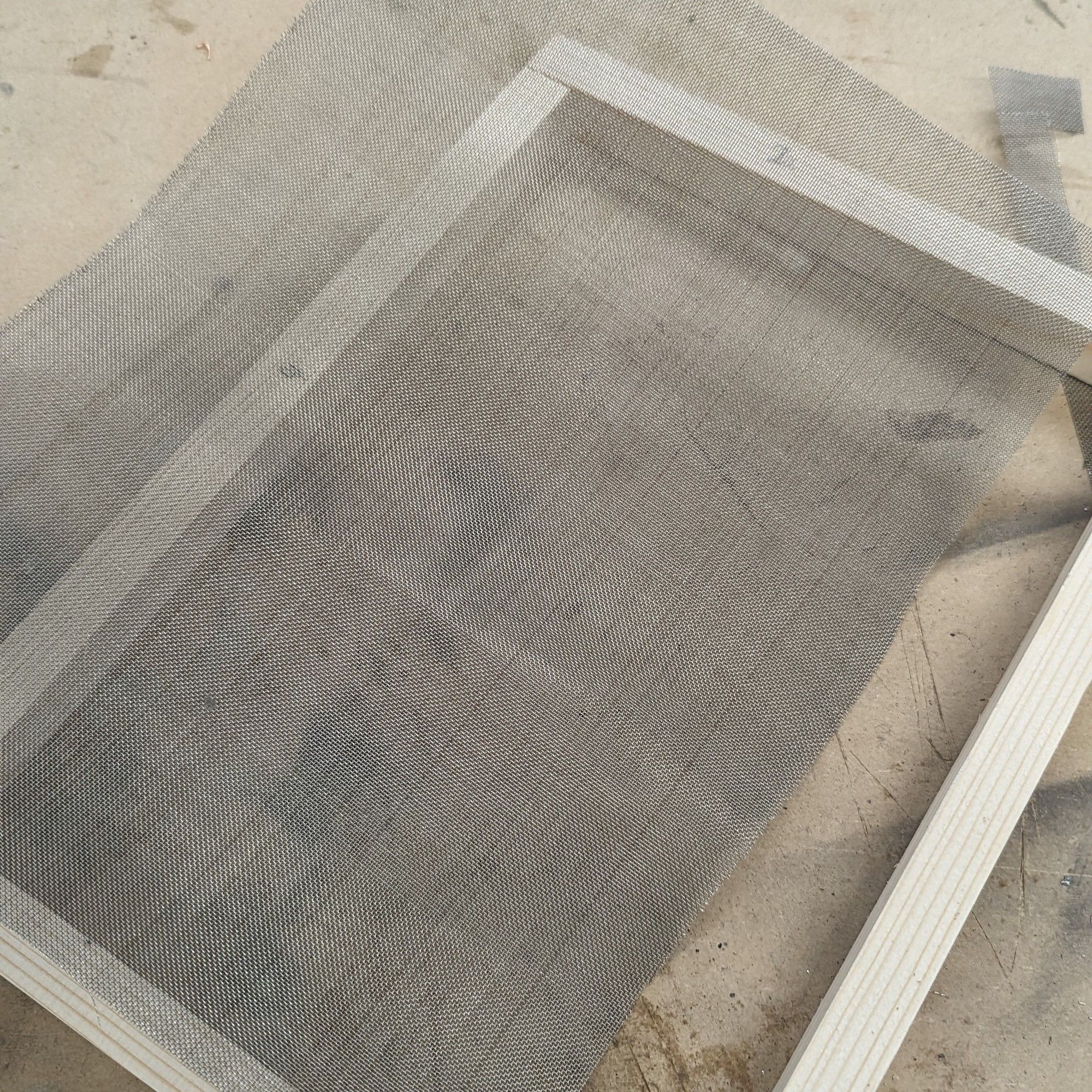 A wooden rectangle frame with a sheet of mesh lying on top of it.