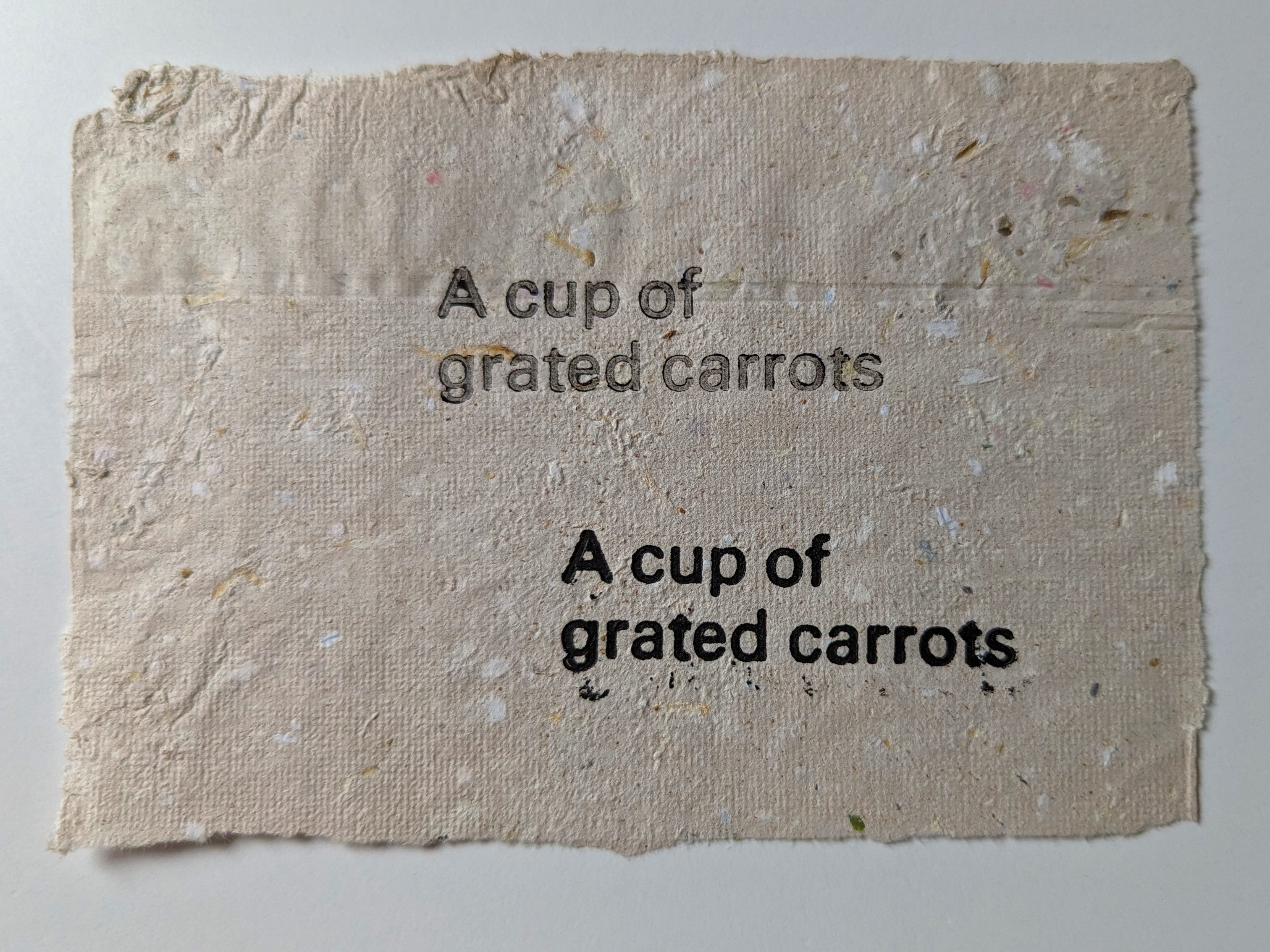A sheet of handmade paper with the phrase "A cup of grated carrots" printed on it twice.