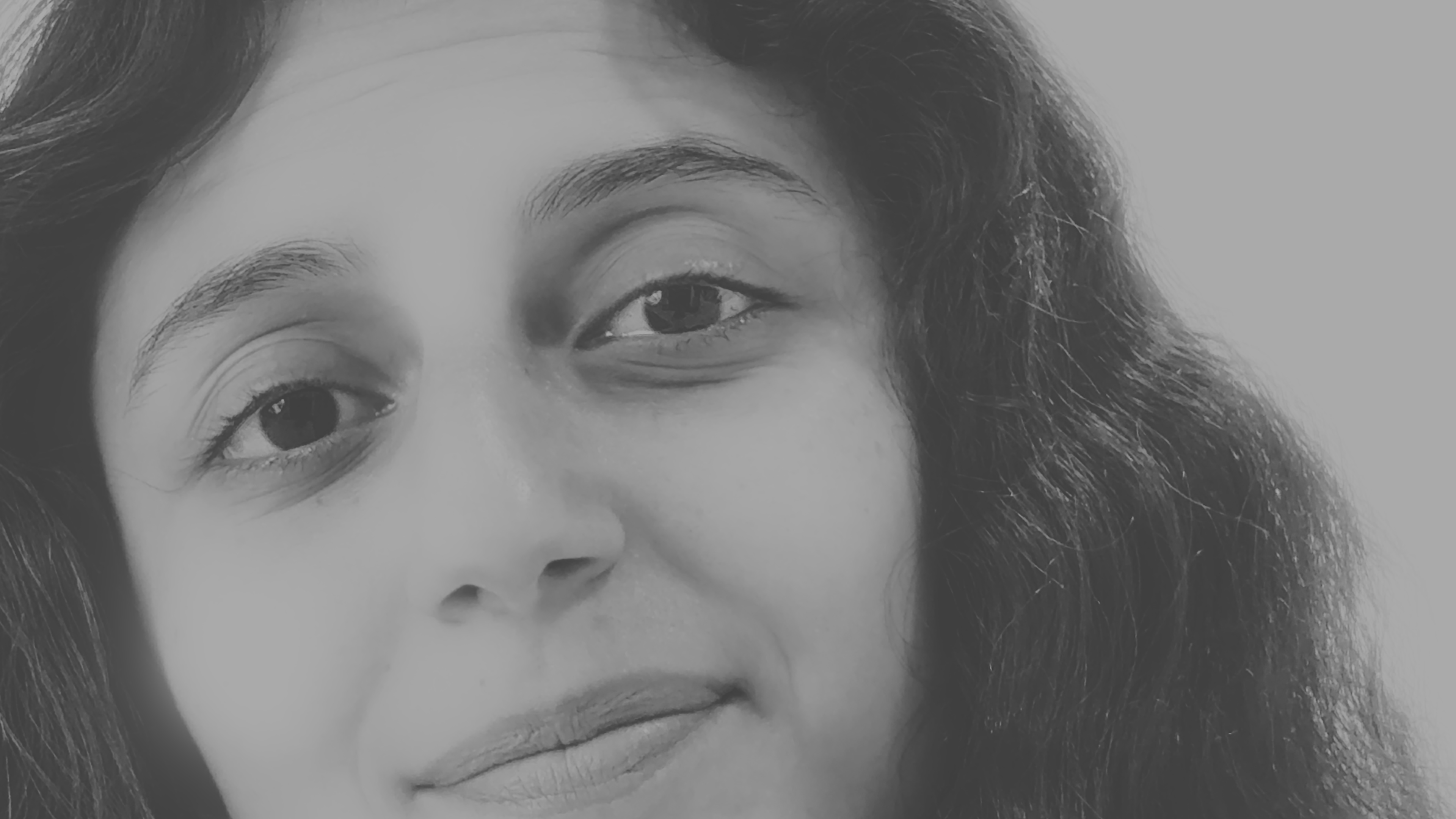 A black-and-white close-up of a young woman’s face with long dark hair against a plain background.