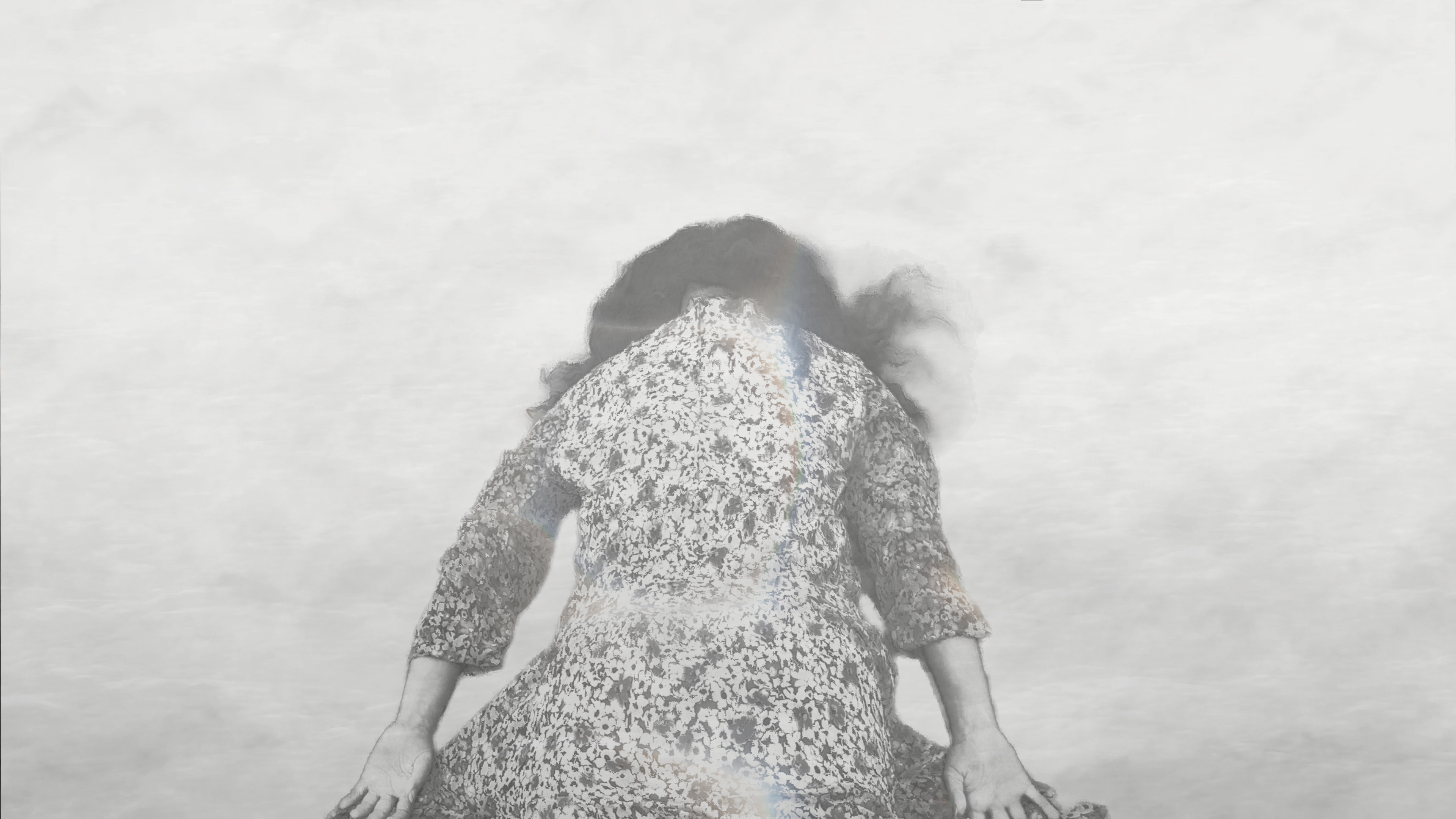A person in a patterned dress lies face down on a pale surface, with long dark hair spread around the head.