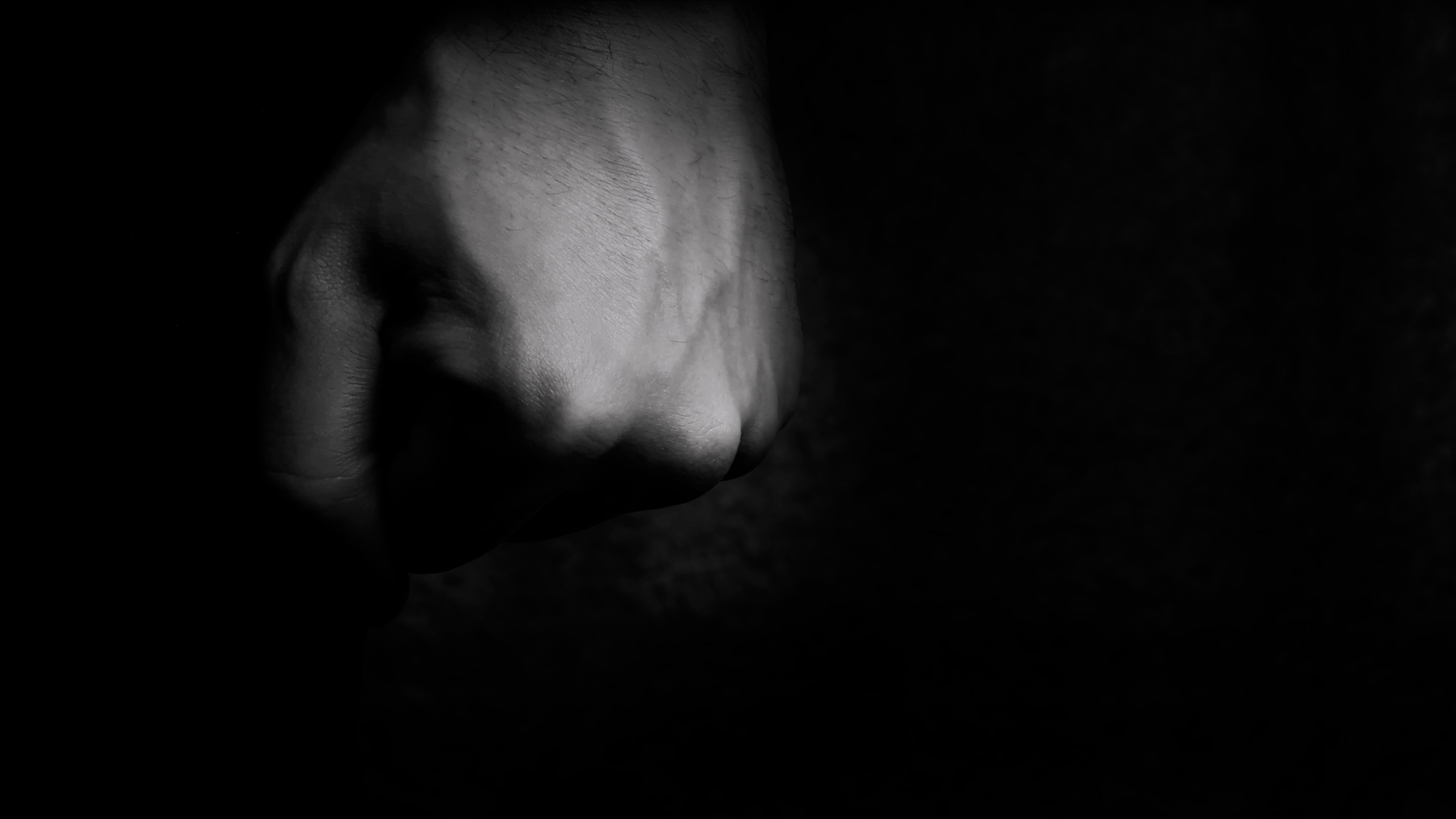 A clenched human fist in black and white against a dark, shadowed background.
