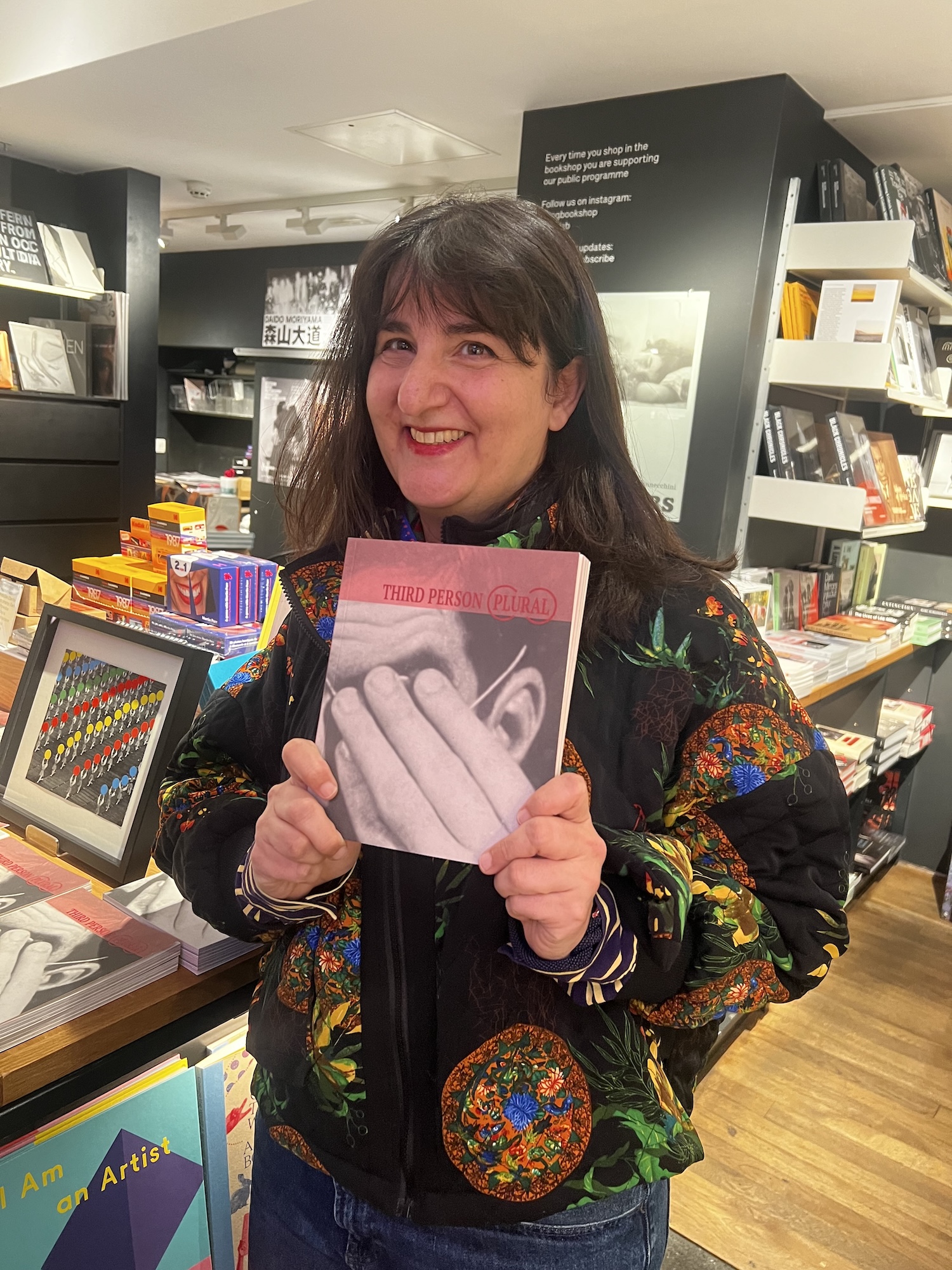 A. Gegisian in a book shop holding up a copy of her book, "Third Person (Plural)"