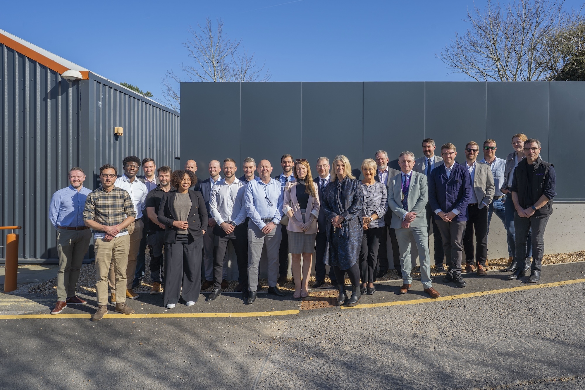 A large group of AUB staff and associates gather outside the on-campus air source heat pumps and pose for a photo