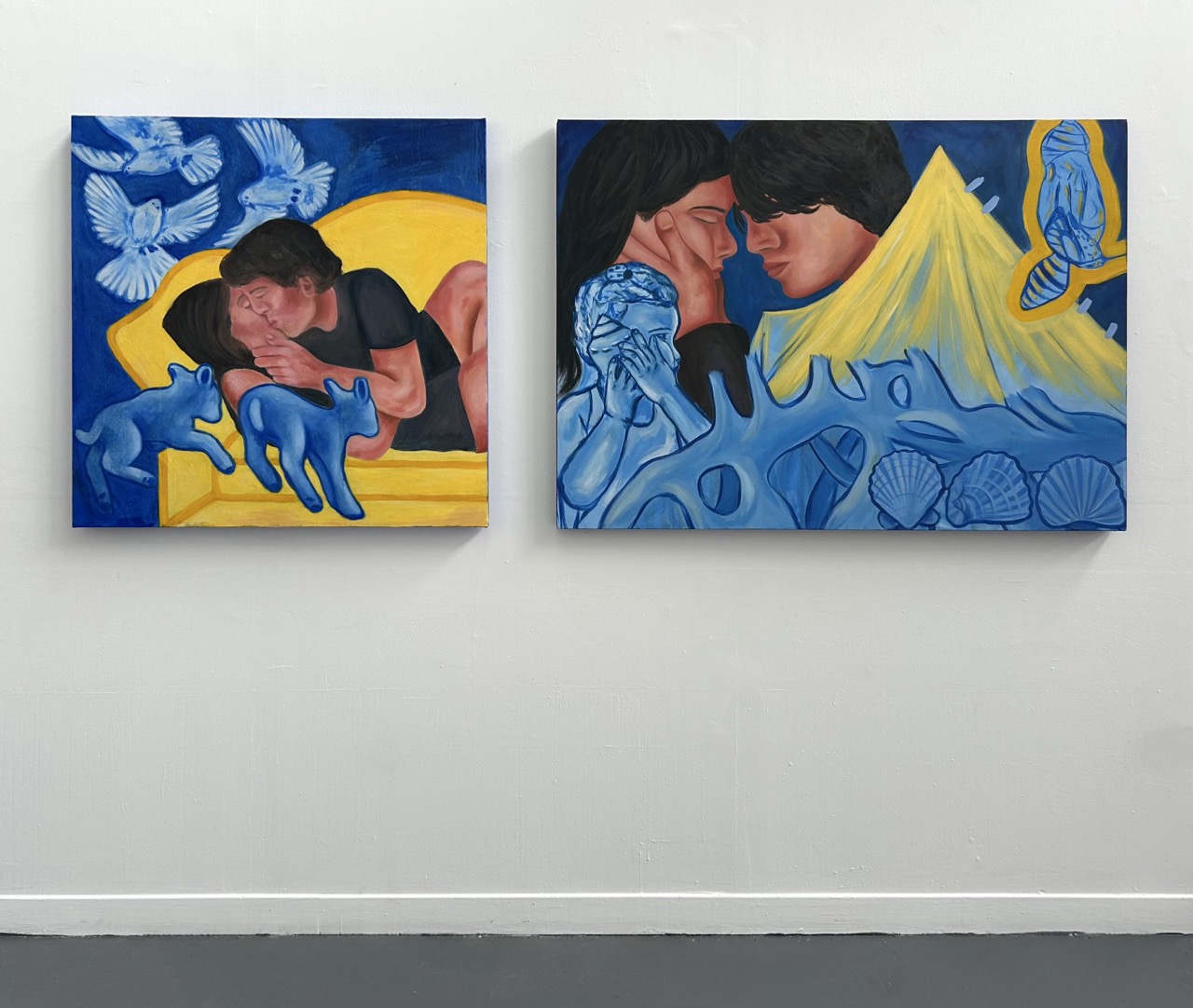 Two colourful paintings displayed on a white wall. The left painting depicts a person reclining on a yellow sofa with two blue cats beside them, while the right painting features two figures touching foreheads with a mountain and shells in the background.