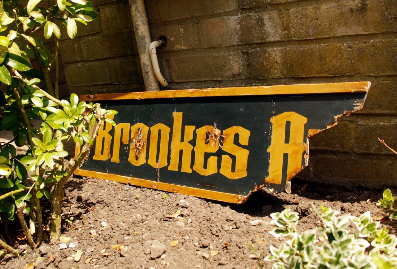 A broken shop sign, with two bullet holes, propped up against the side of a building.
