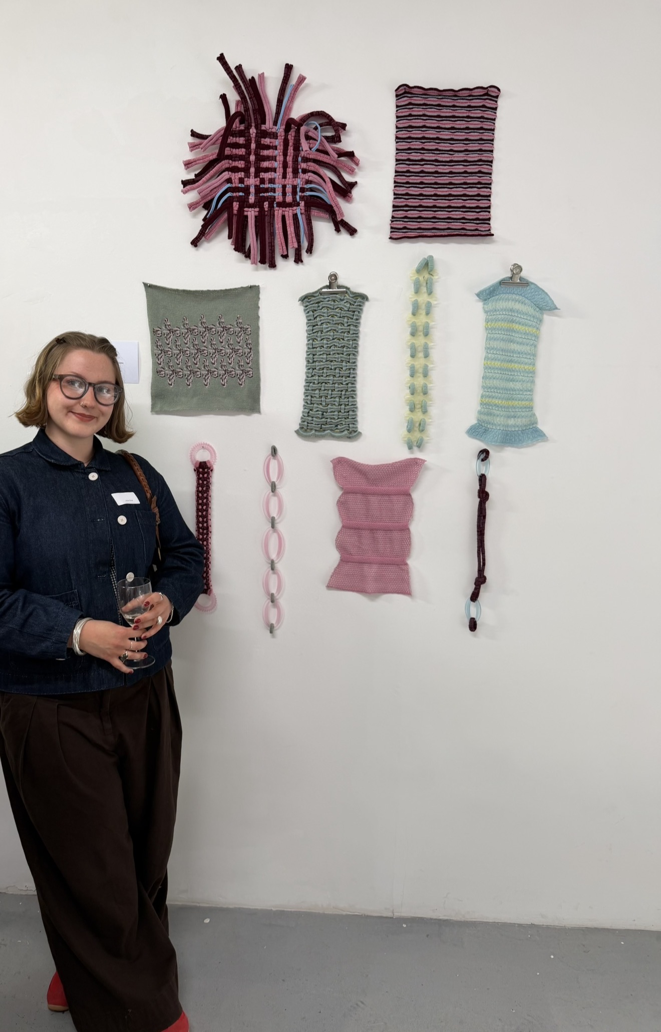 BA (Hons) Textiles Design A. Rose standing next to a display of textiles work on a gallery wall.