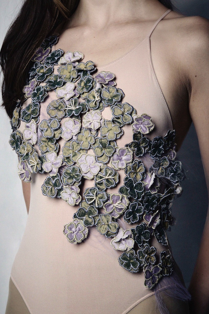Person wearing decorative top made of clustered fabric flowers in purple, green, and dark tones arranged in organic pattern.